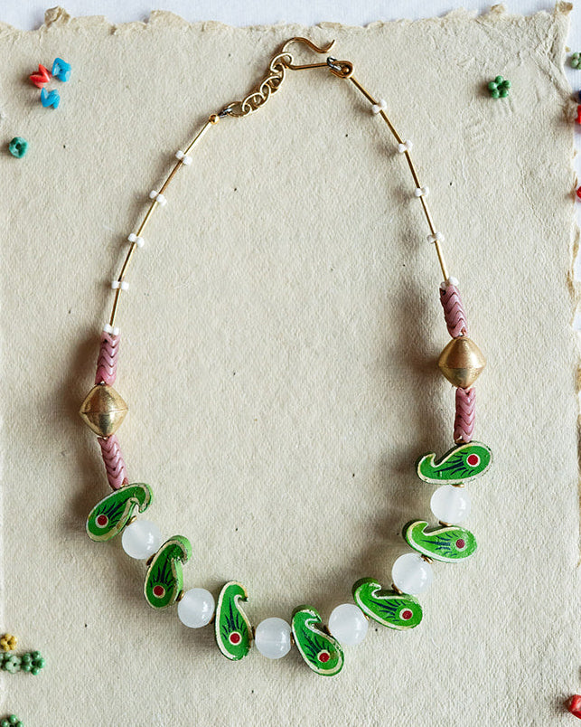 Necklace with green and white beads on a textured card against a black and white patterned background.