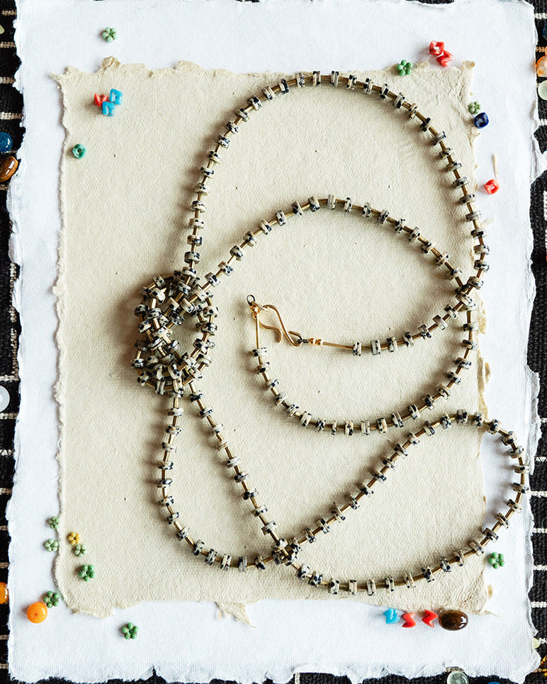 Three beaded necklaces on a textured white card with a black and white geometric patterned background.