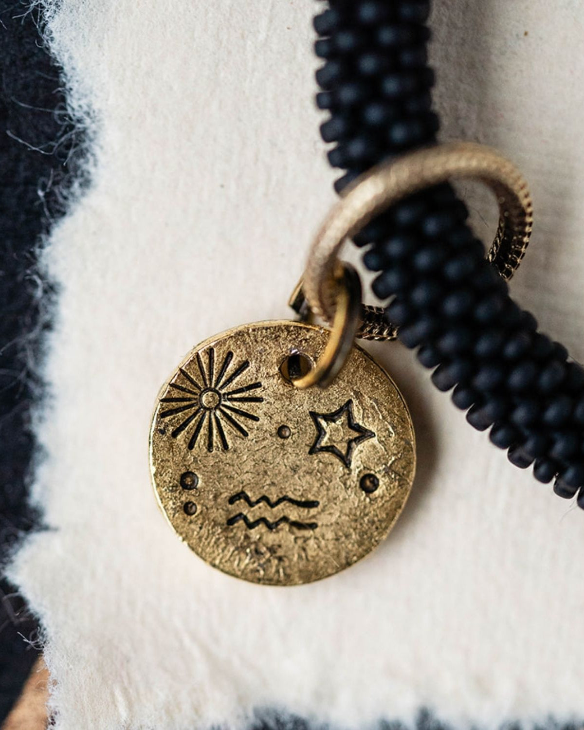 Close-up detail of gold Aquarius zodiac charm showing engraved sun starburst star and water bearer waves