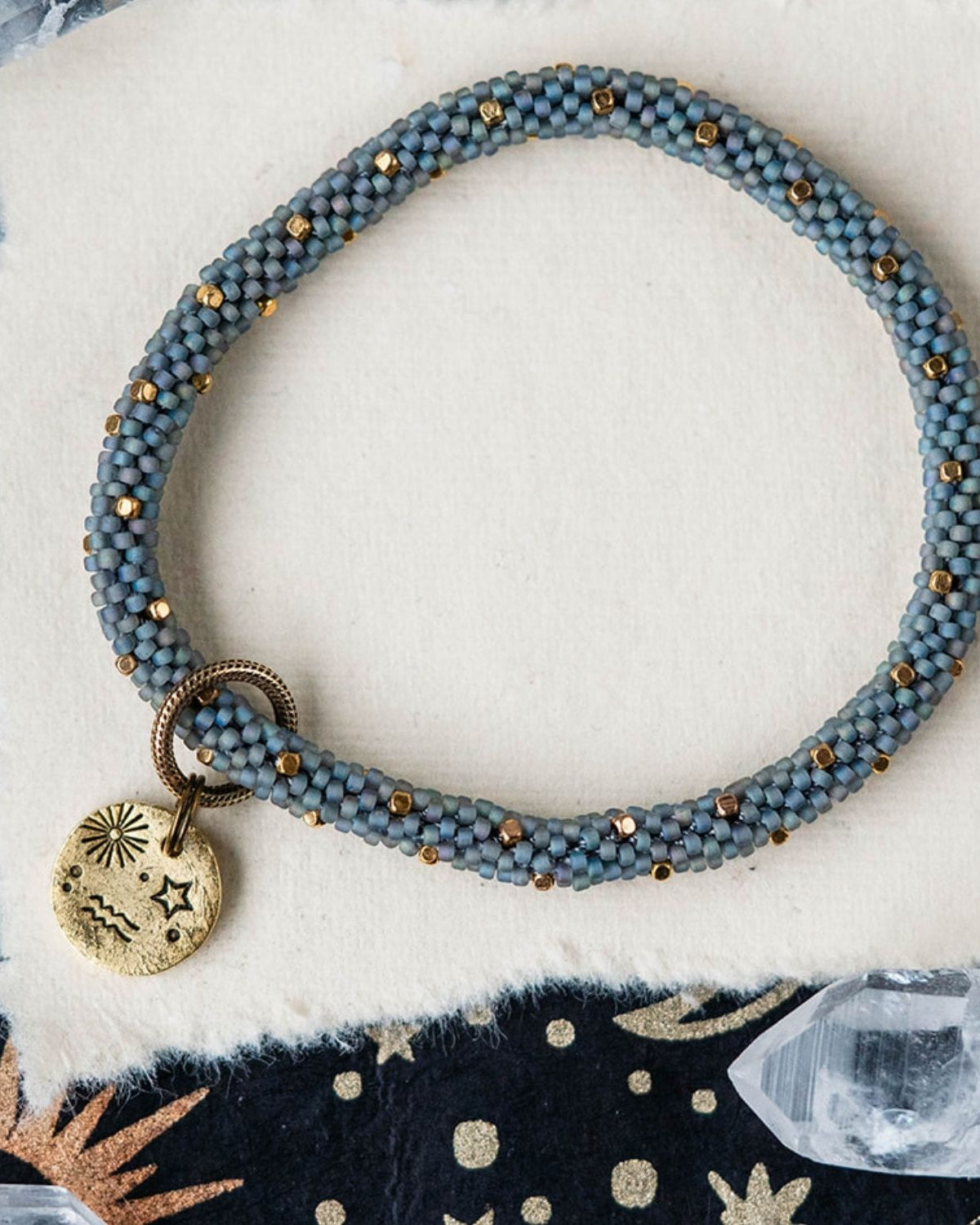 Blue-grey beaded bracelet with gold spacer beads and Aquarius zodiac charm on celestial background