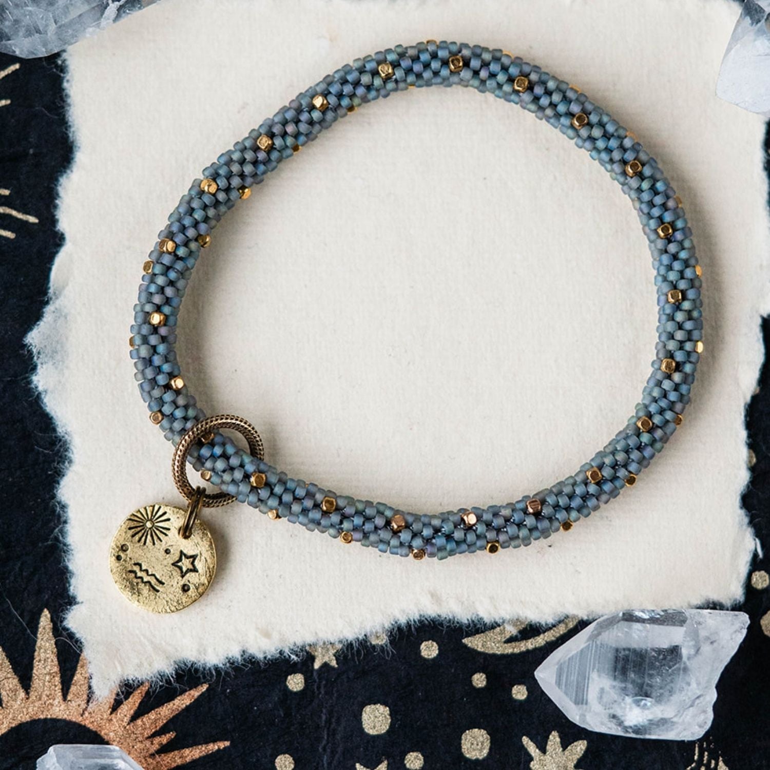 Blue-grey beaded bracelet with gold spacer beads and Aquarius zodiac charm on celestial background