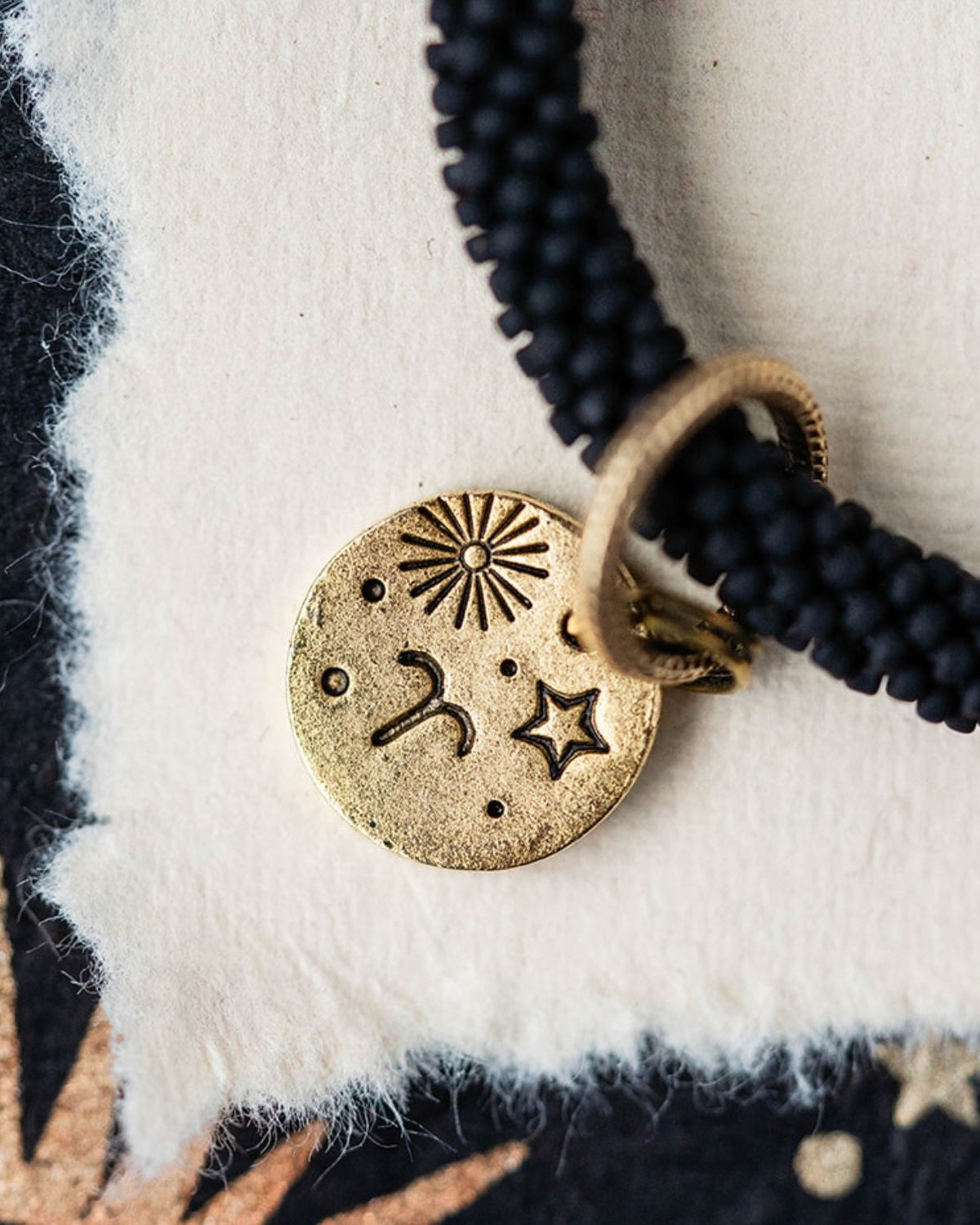 Close-up gold Aries zodiac charm with ram horn engravings attached to black beaded jewelry