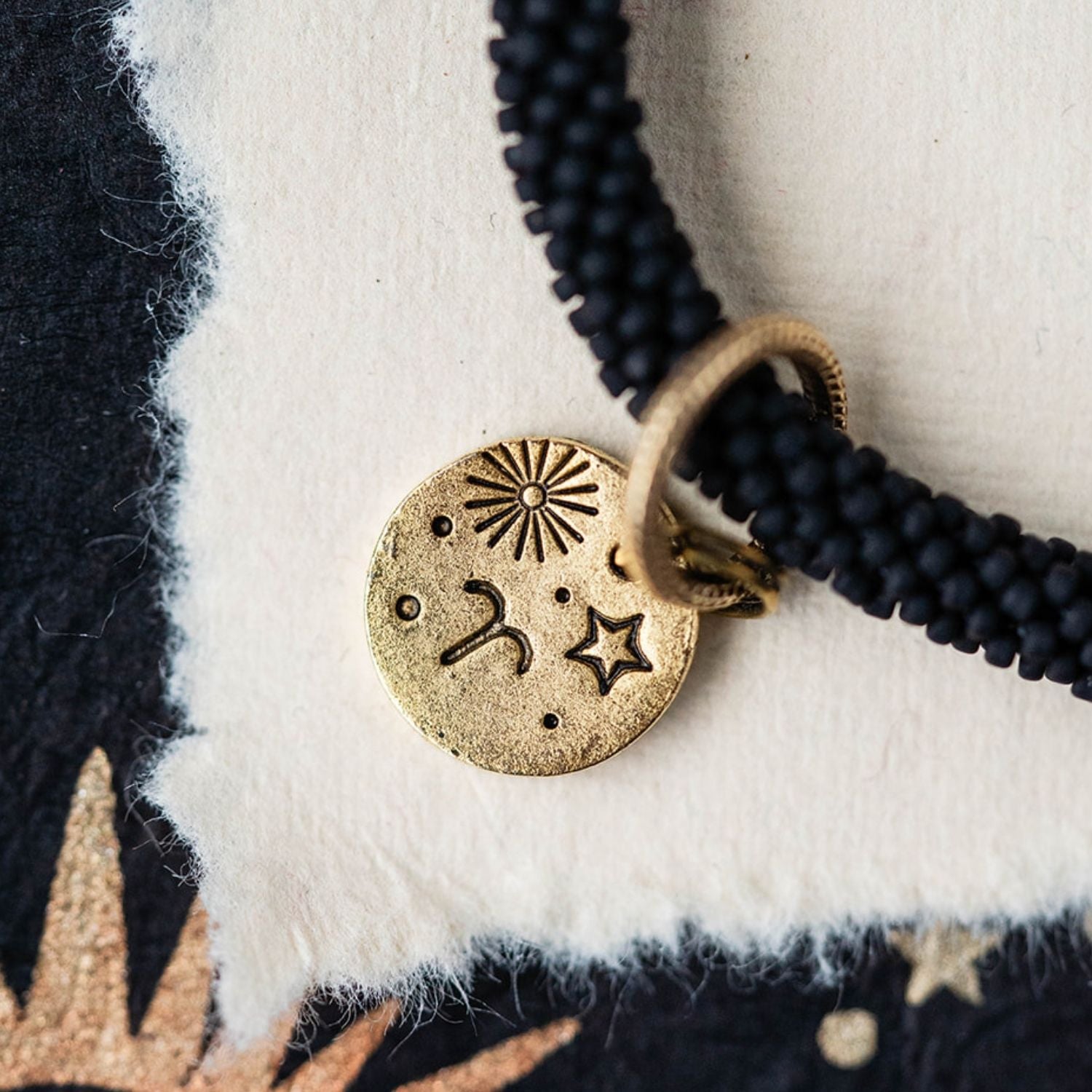 Close-up gold Aries zodiac charm with ram horn engravings attached to black beaded jewelry