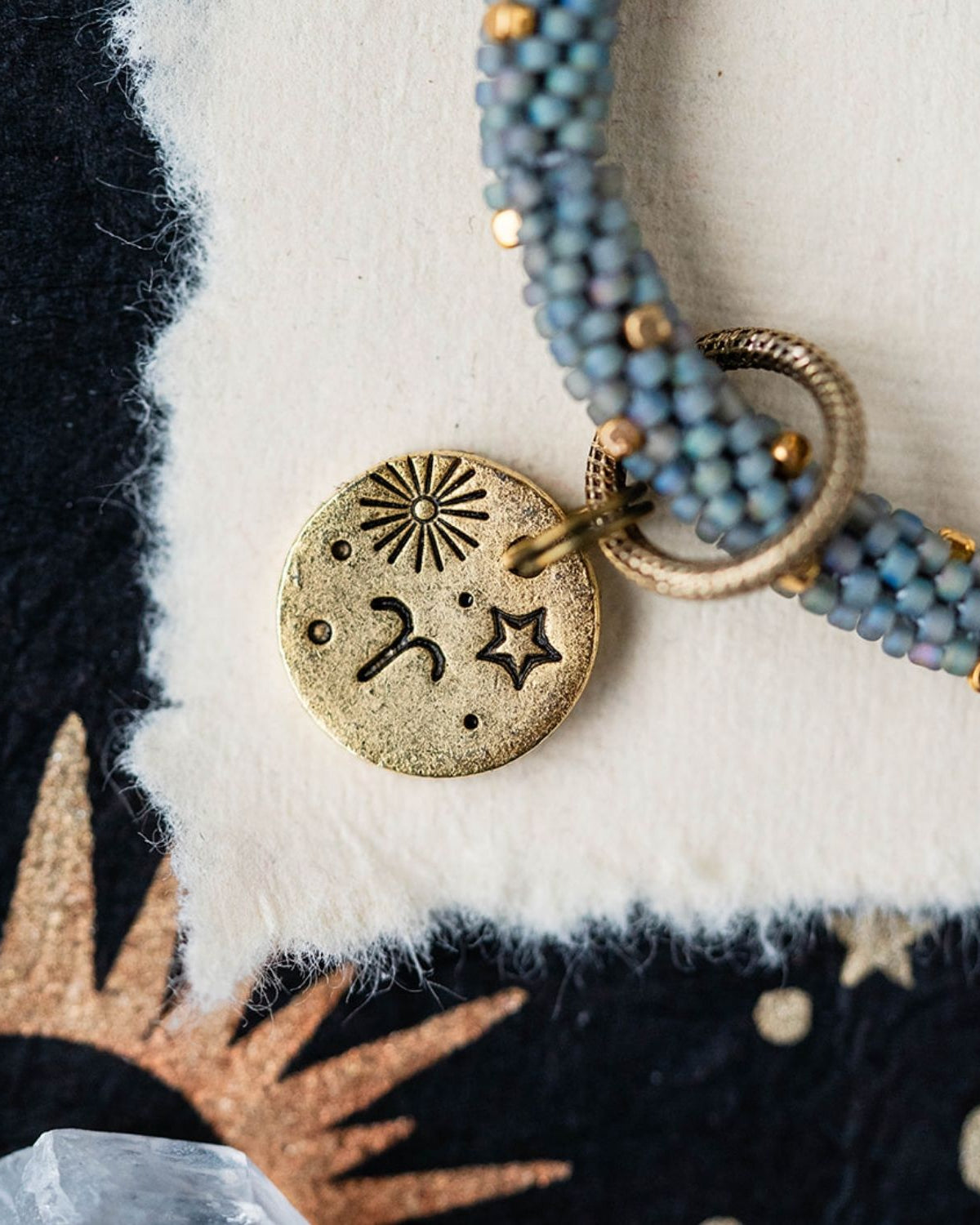 Gold Aries charm with blue-grey beaded strands showing sun and ram horn celestial engravings