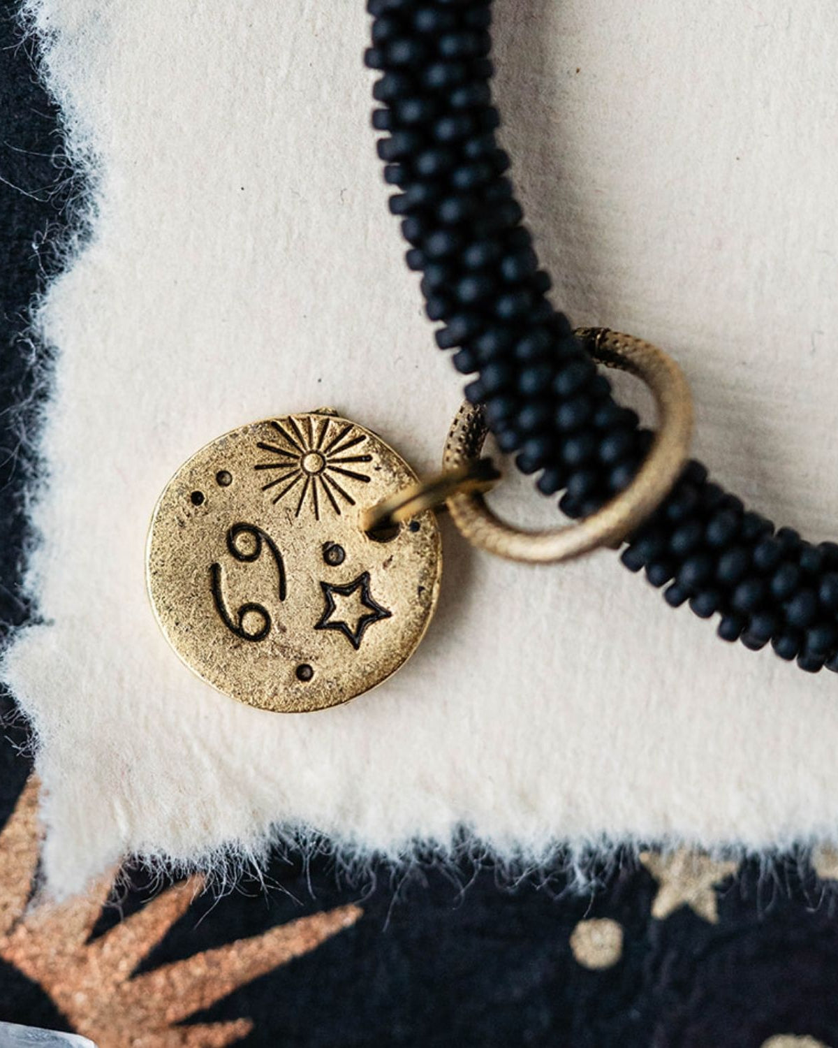 Close-up Cancer zodiac charm with crab engravings attached to black beaded bracelet detail