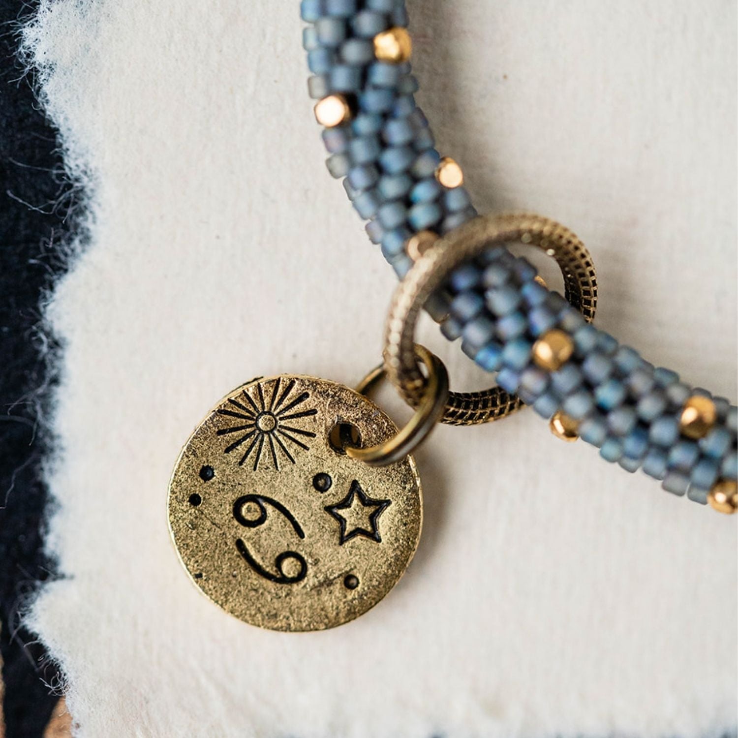 Gold Cancer charm with blue-grey beaded jewelry showing crab constellation and sun engravings