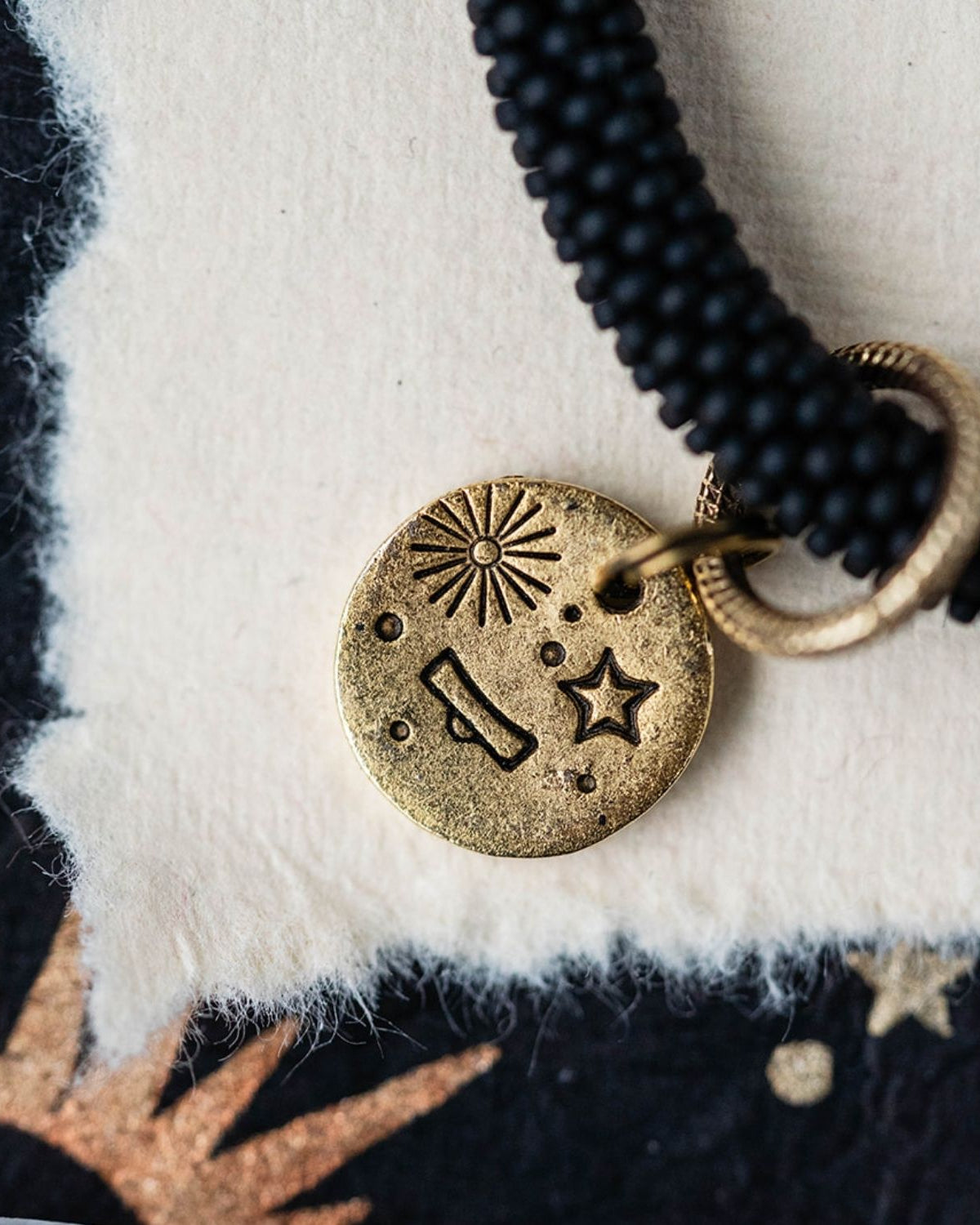 Close-up gold Libra zodiac charm with scales symbol attached to black beaded jewelry