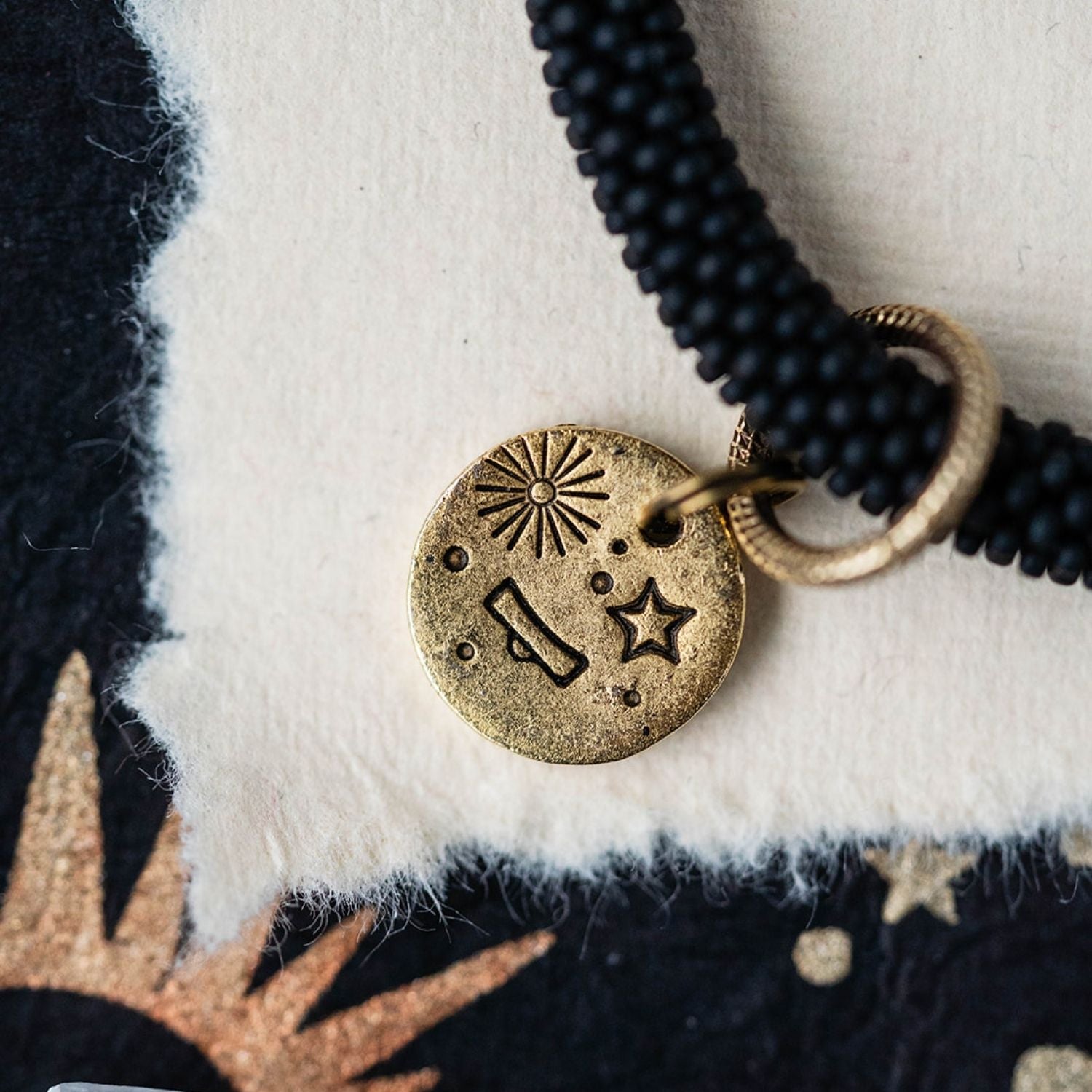Close-up gold Libra zodiac charm with scales symbol attached to black beaded jewelry