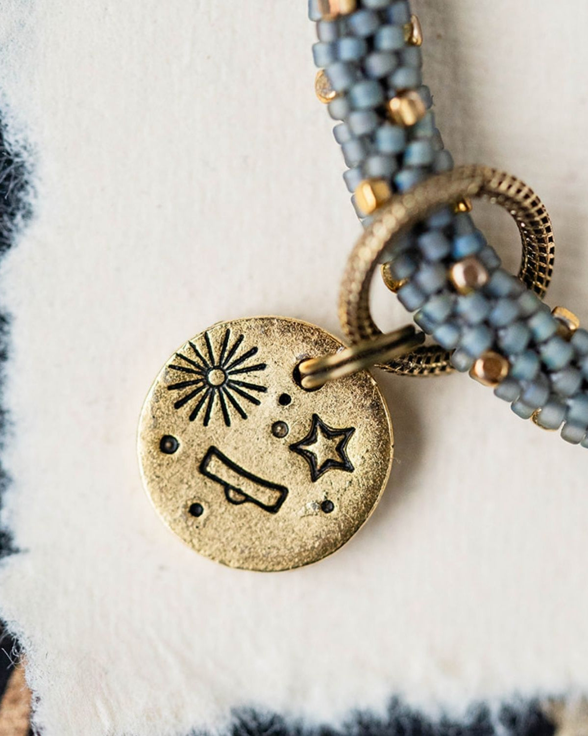 Gold Libra charm with blue-grey beaded strands showing scales constellation and sun engravings