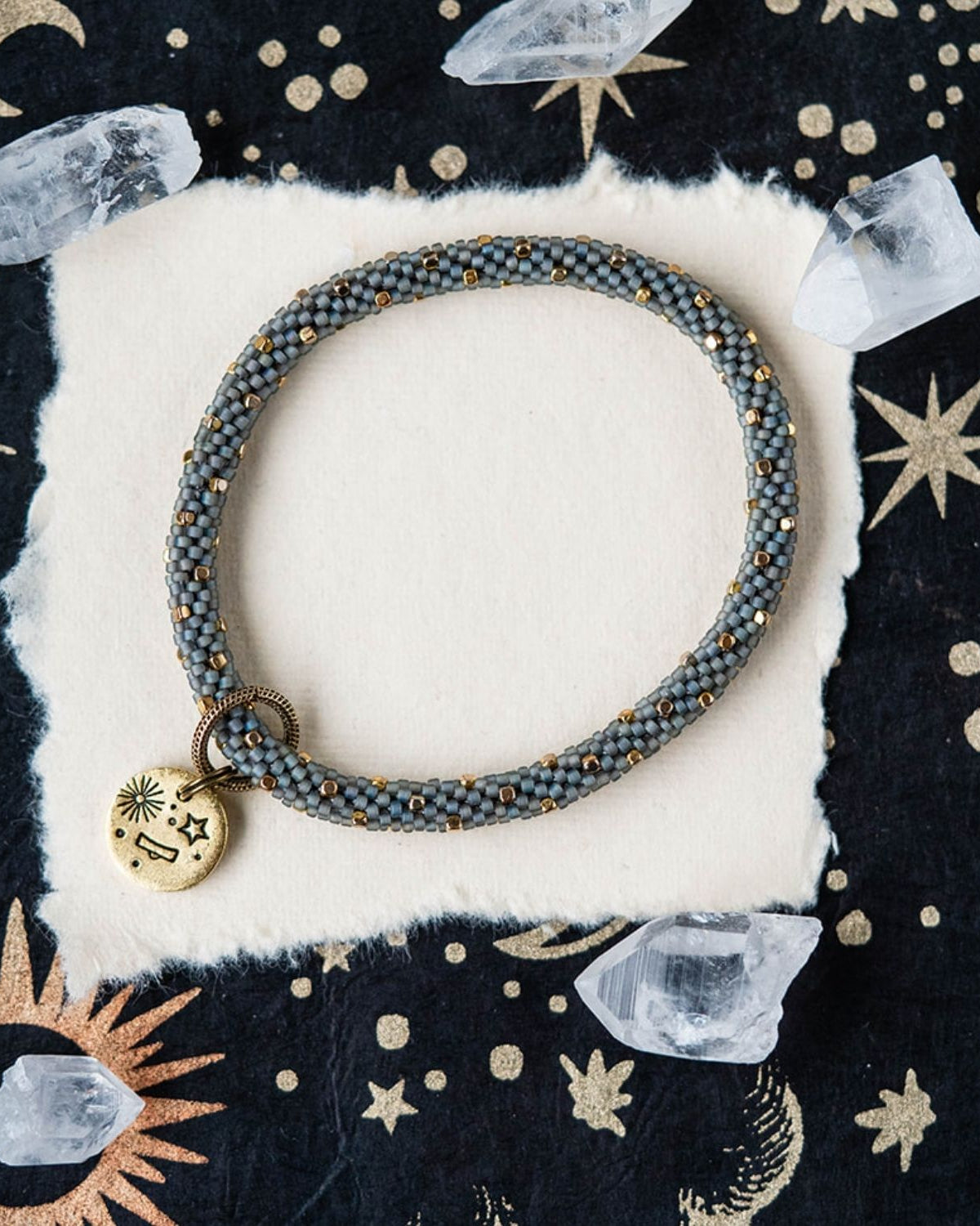 Blue-grey beaded bracelet with gold accents and Libra zodiac charm on celestial background