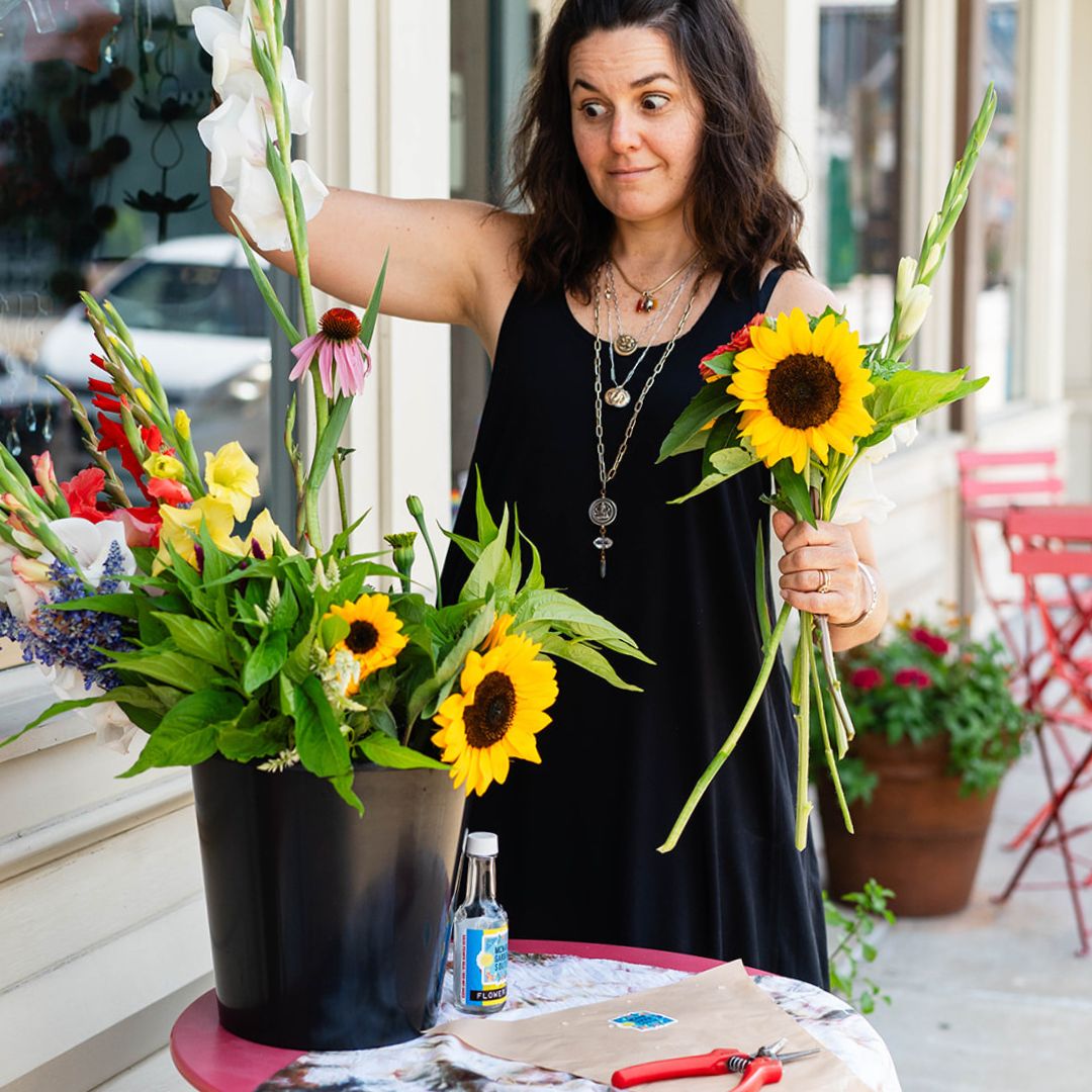 Brandy arranging a flower bouquet featuring sunflowers, gladiolus, and more for Bella Vita’s Summer Subscription.