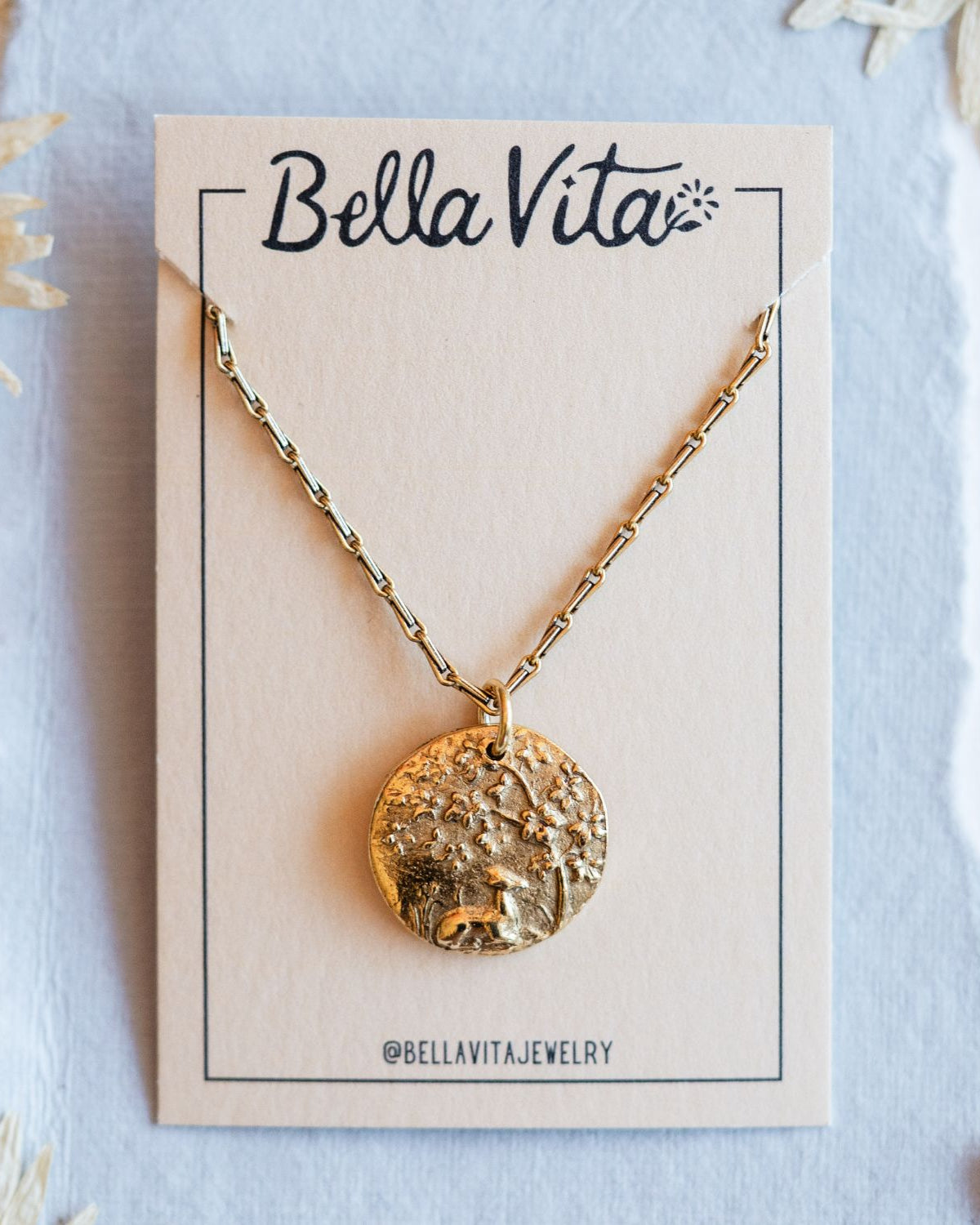 Gold cast fawn heirloom pendant displayed on Bella Vita branded card with daisy flowers