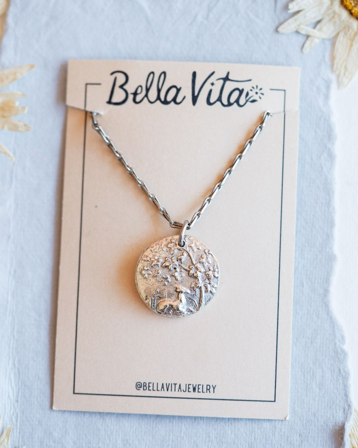 Silver cast fawn heirloom pendant shown with Bella Vita artisan jewelry packaging and daisies