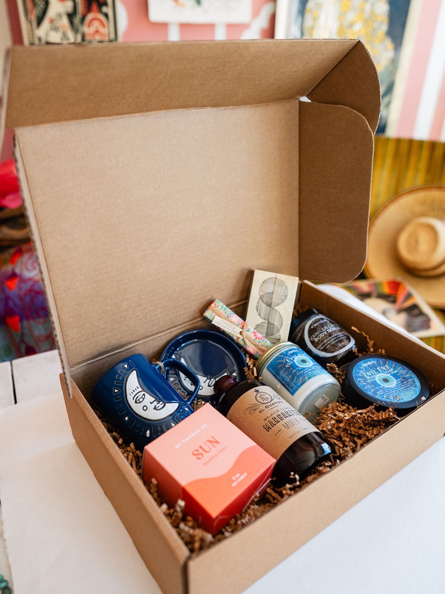 Bella Vita custom gift box with Evil Eye body butter, whipped soap, El Guapo mixer, Sun candle, and blue face mugs displayed at an angle