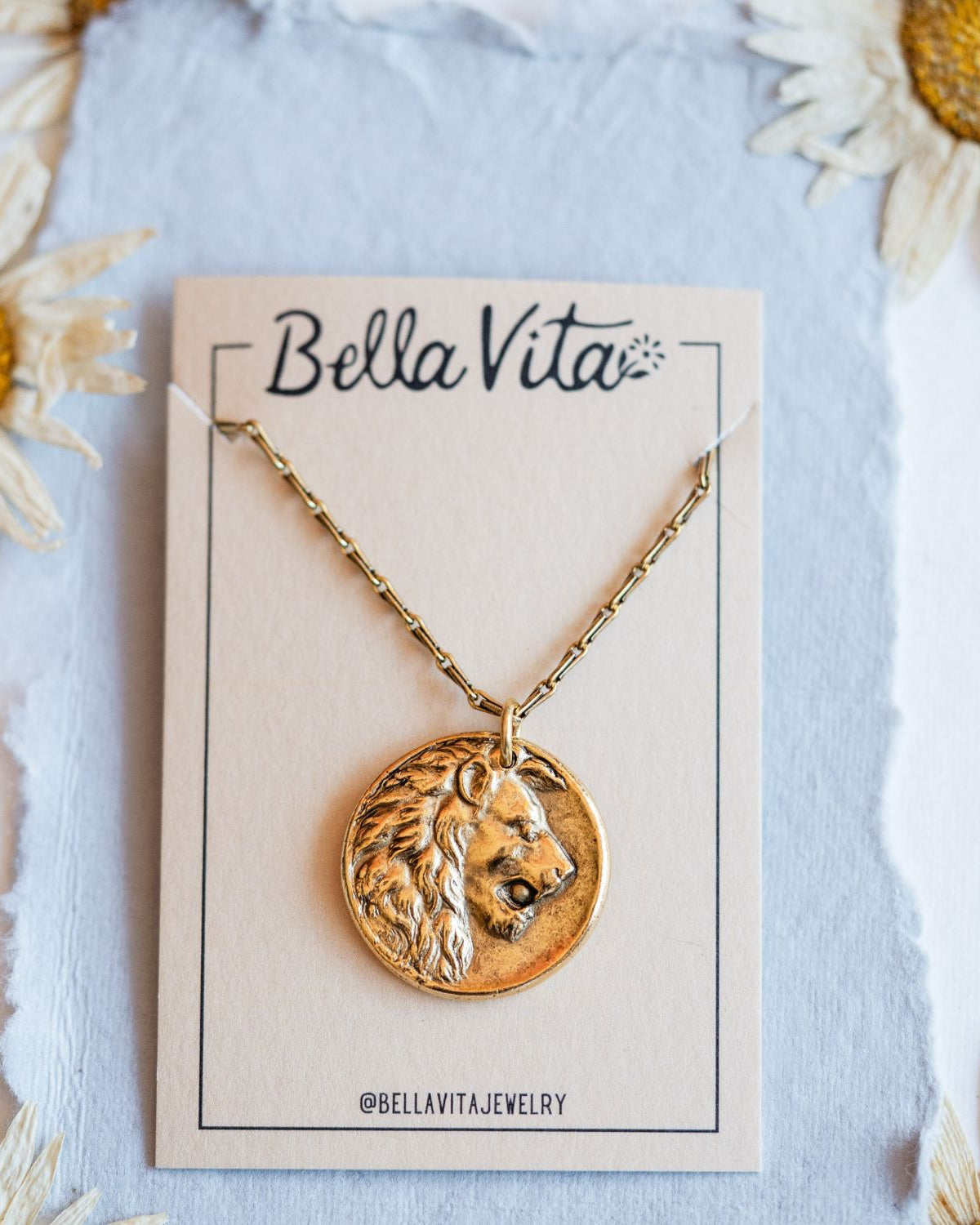 Gold cast lion heirloom pendant displayed on Bella Vita branded card with daisy flowers