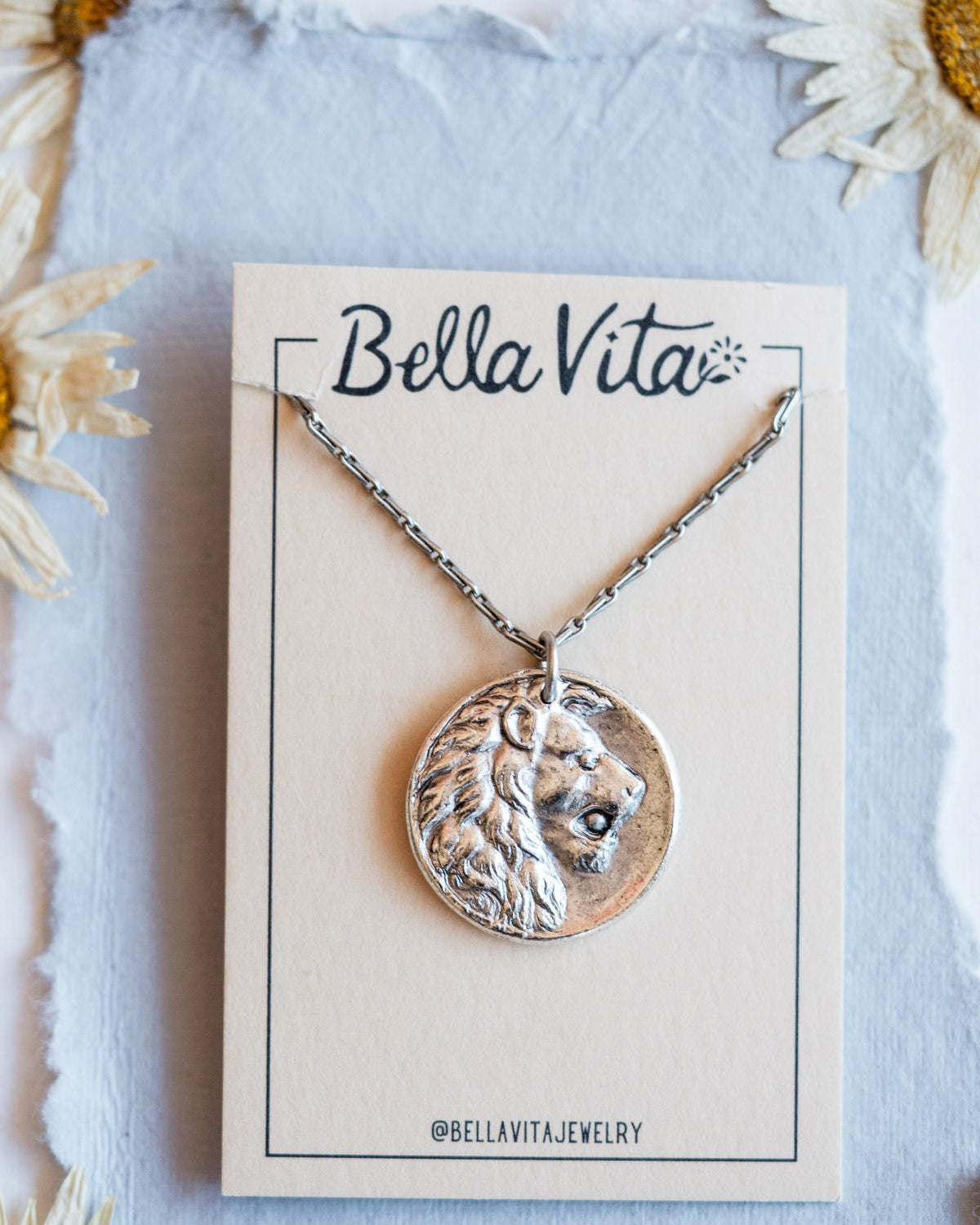 Silver cast lion heirloom pendant shown with Bella Vita artisan jewelry packaging and daisies