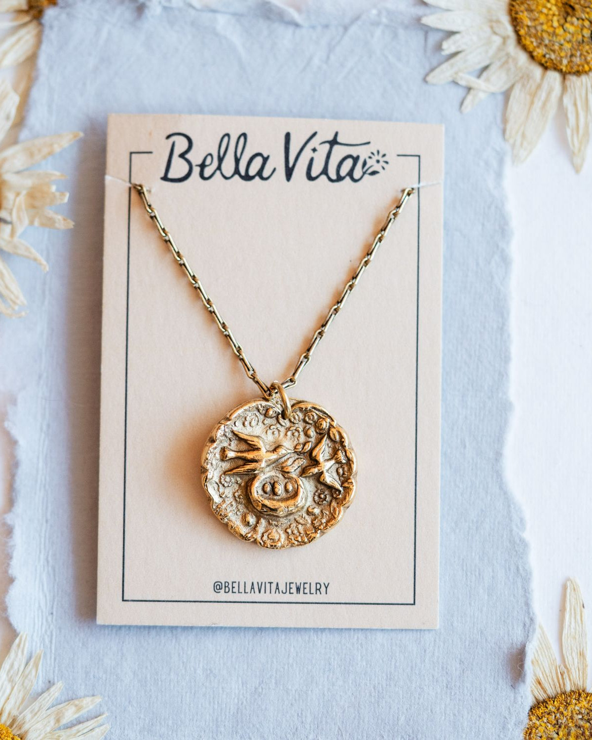 Gold cast mama bird heirloom pendant displayed on Bella Vita branded card with daisy flowers