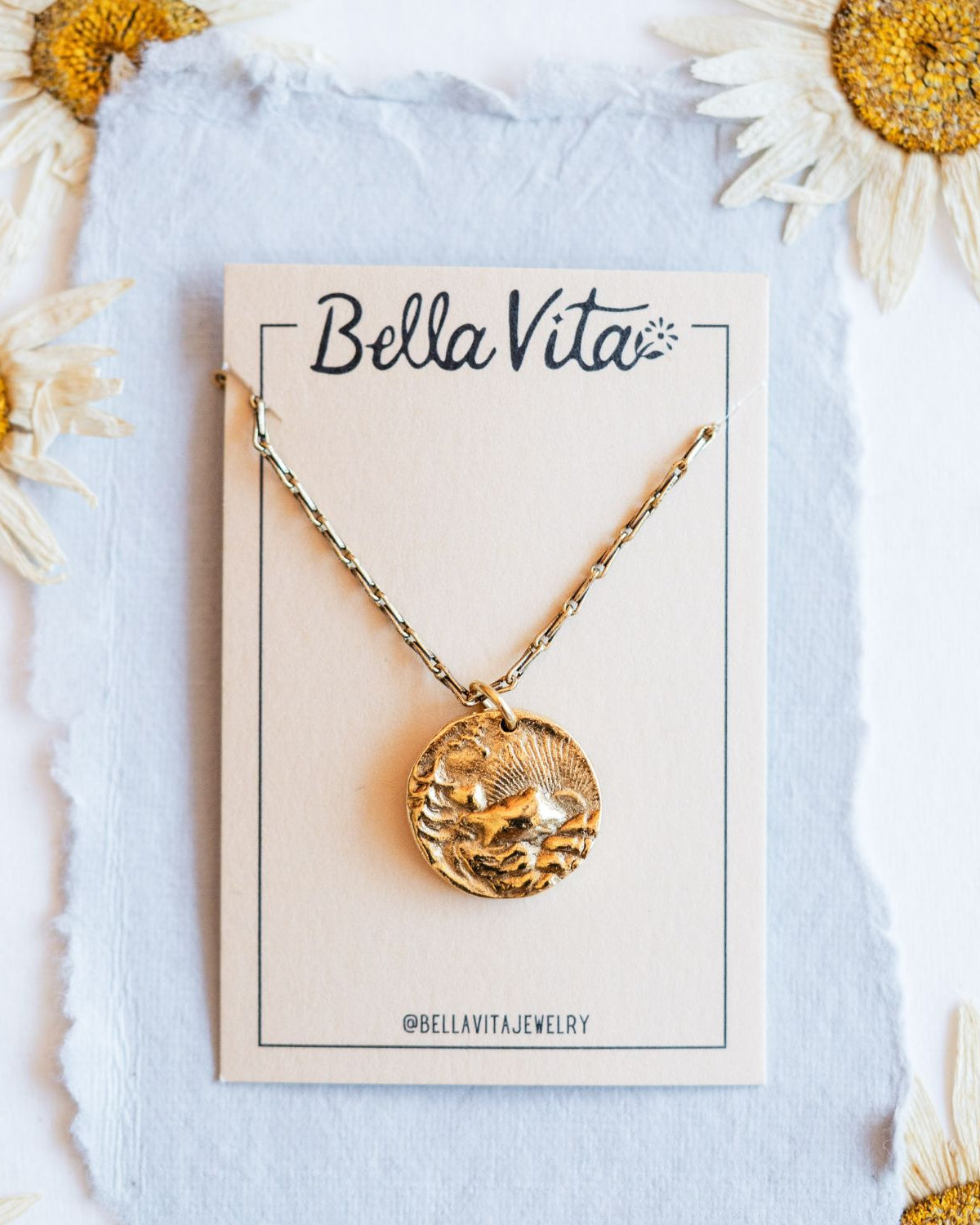 Gold cast mountain sunset heirloom pendant on Bella Vita branded card with daisy flowers