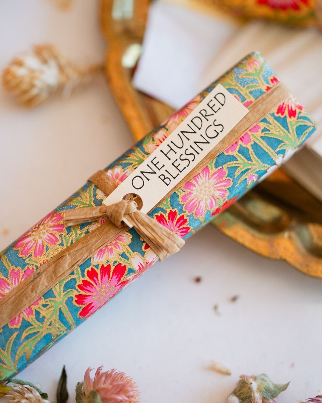 Close-up of 100 Blessings affirmation cards in vibrant floral wrapping with kraft gift tag on white surface.