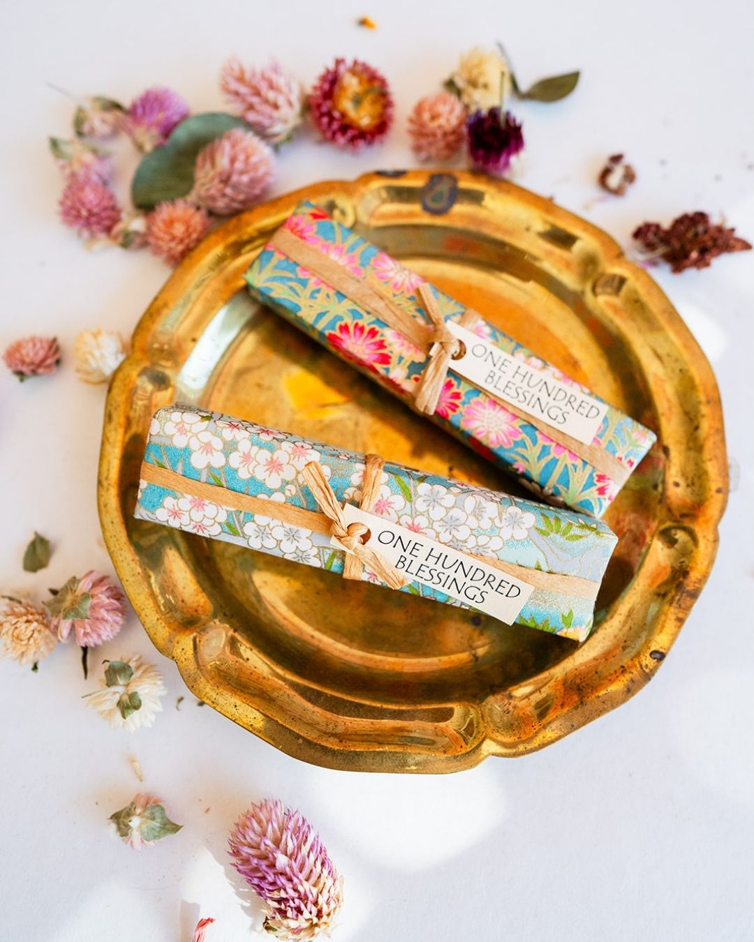 100 Blessings affirmation bundle with colorful floral wrapping displayed on gold tray with dried flowers.