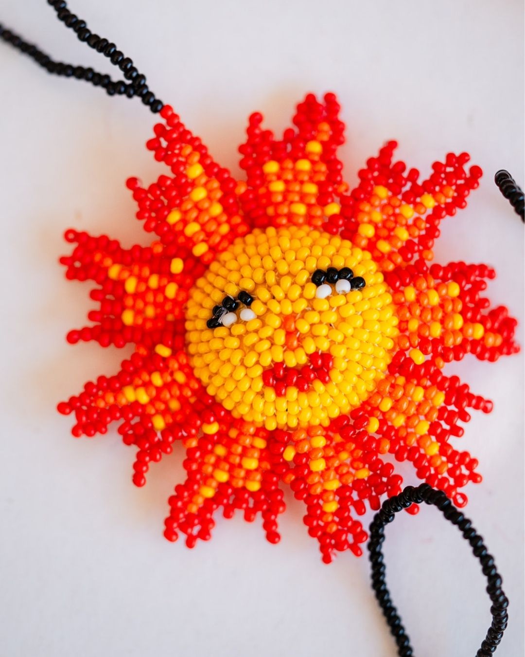 Close-up of beaded sunshine ornament with orange and yellow seed beads, smiling face and hanging cord