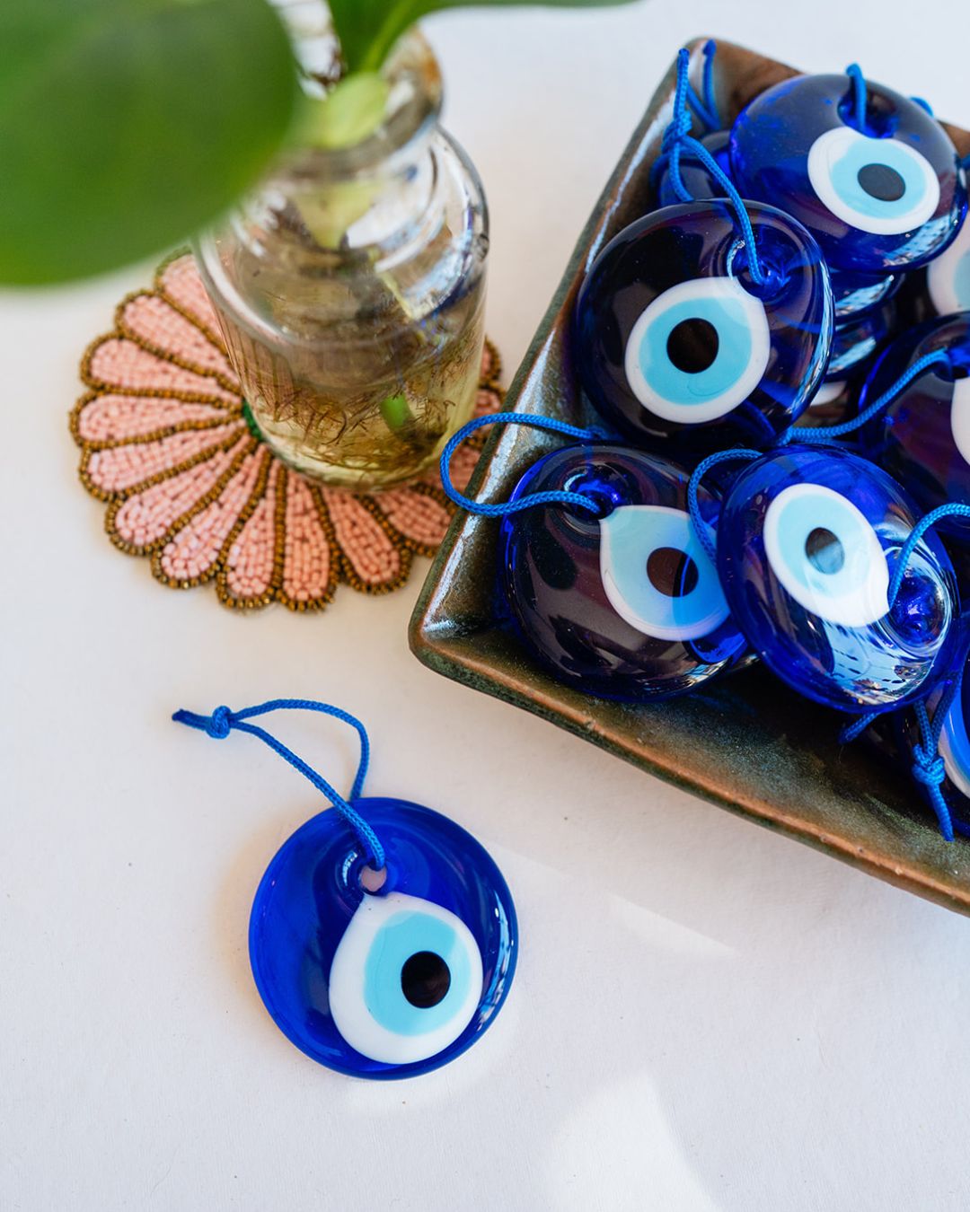 Traditional blue glass evil eye talismans in wooden box with single charm displayed and small plant for protection decor.