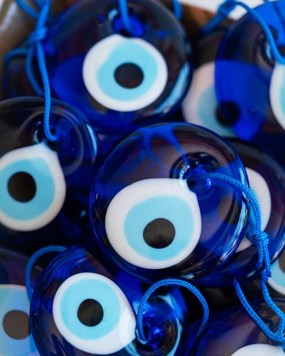 Close-up of deep blue glass evil eye talismans with white and light blue concentric circles on dark cords.