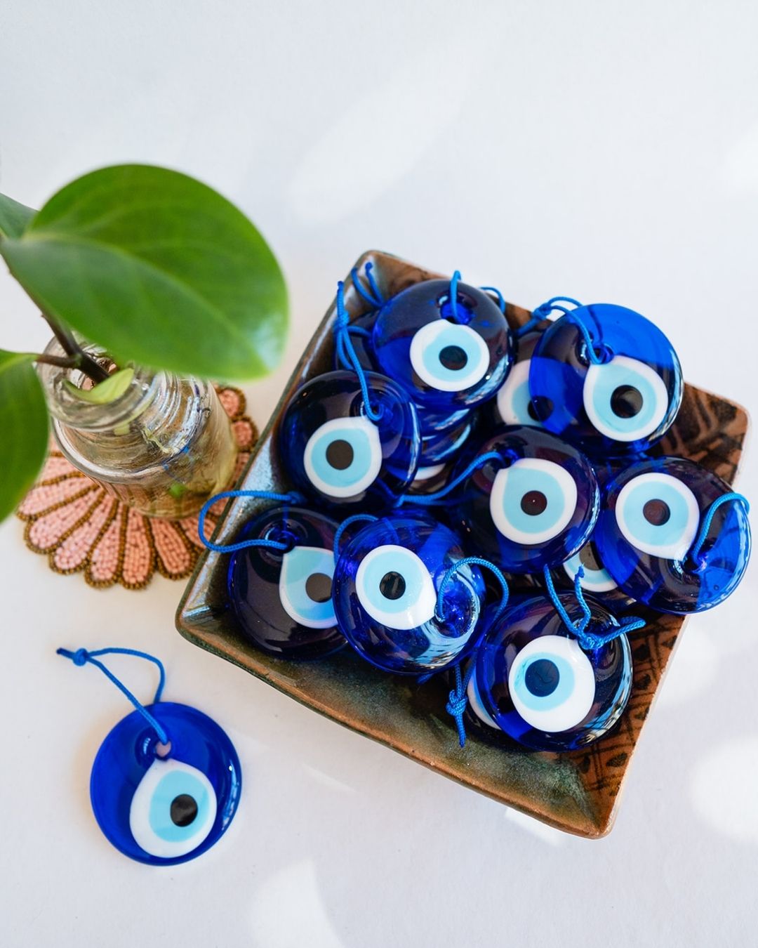 Blue glass evil eye protection talismans in decorative box with plant and beaded coaster - traditional protection symbols.