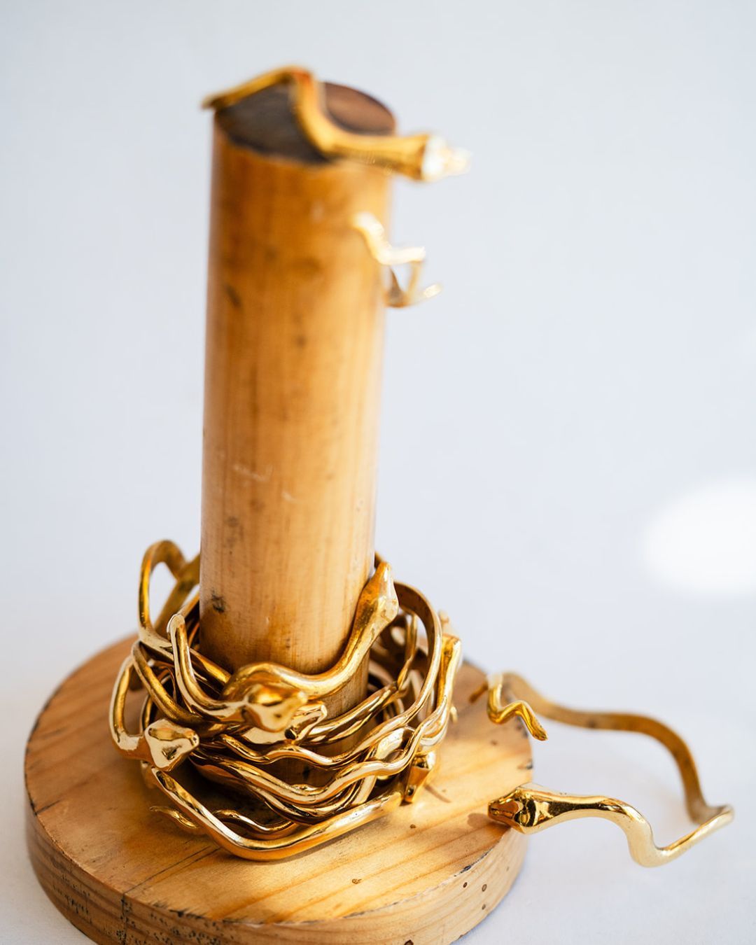 Shiny brass serpent cuff displayed on wooden stand showing the coiled design