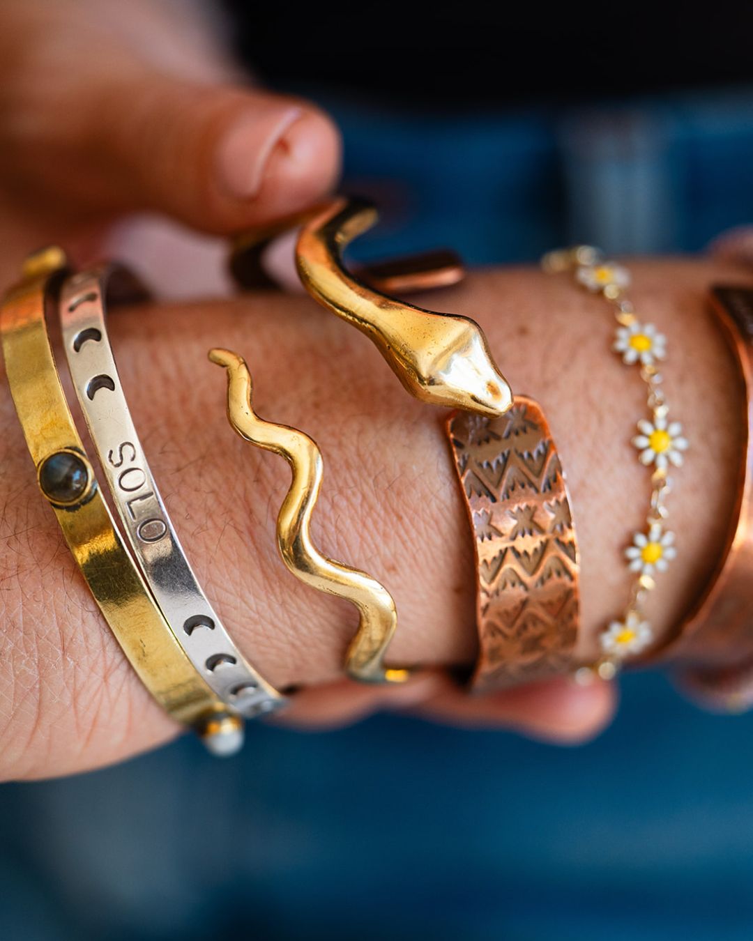 Hand wearing shiny brass serpent cuff stacked with other artisan bracelets