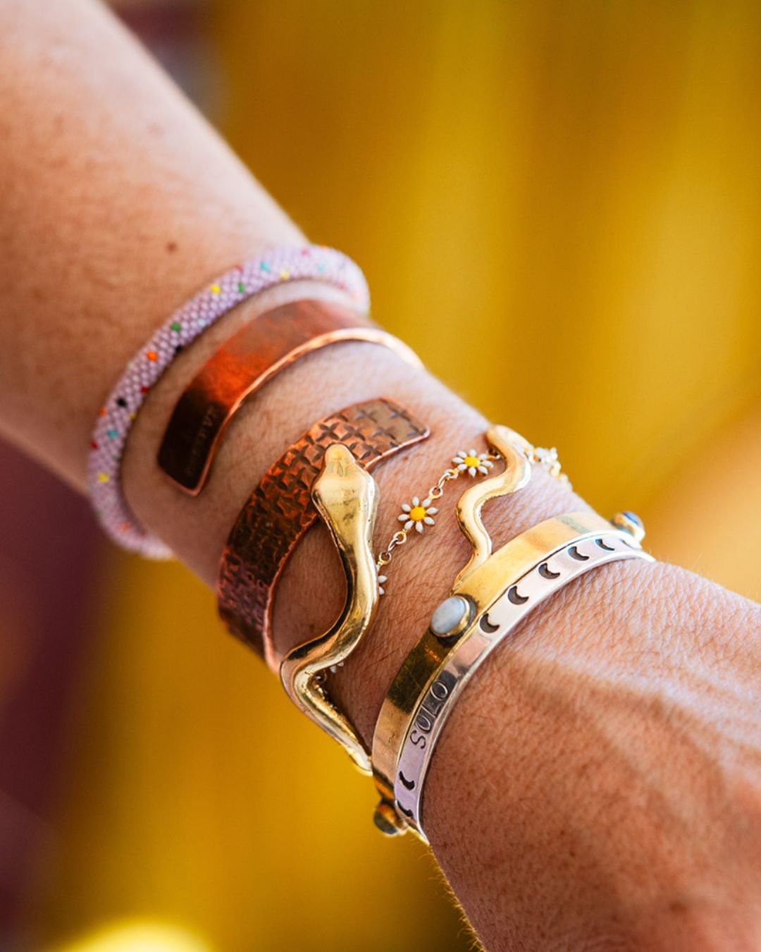 Brass serpent cuff styled with mixed metal bracelets against yellow background