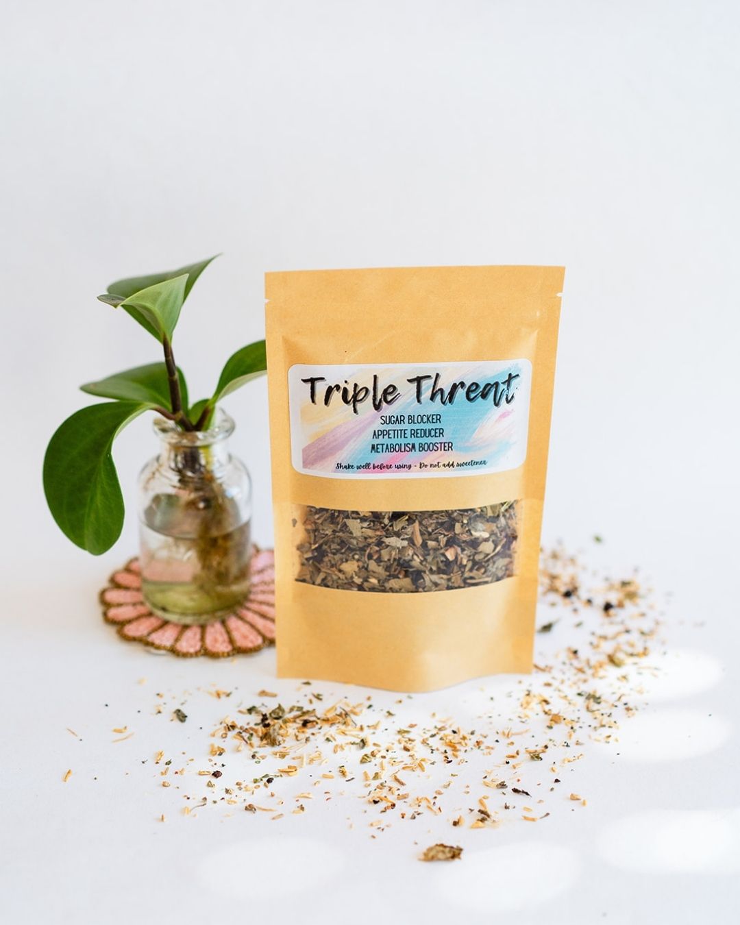 BWG Triple Threat tea blend in kraft packet displayed with small plant in water on beaded coaster.