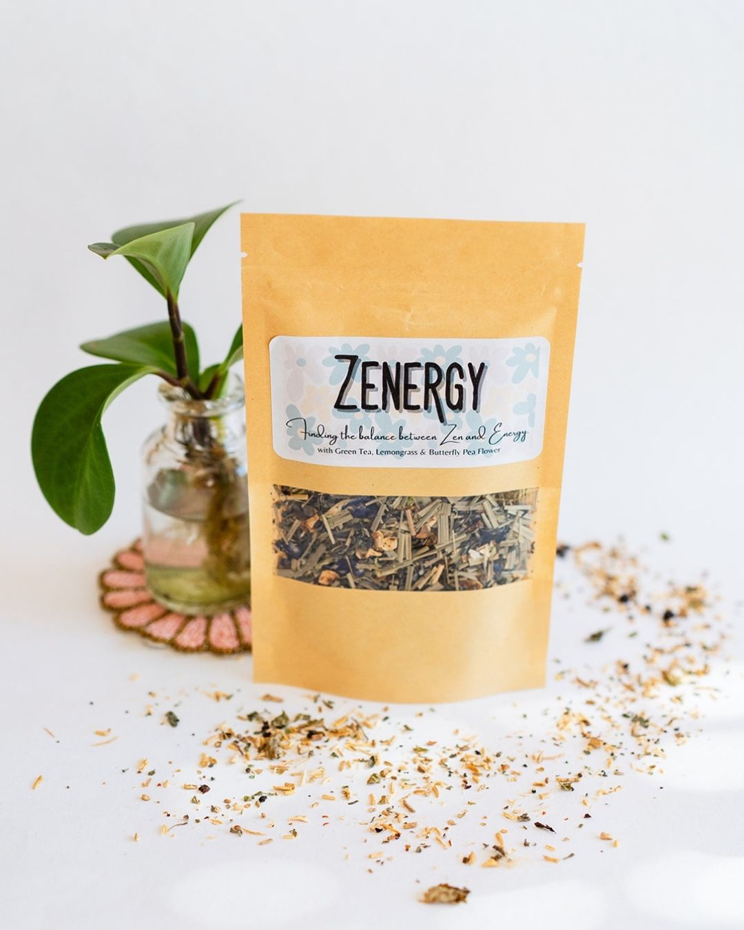 BWG Zenergy tea blend in kraft paper packet with potted plant on beaded coaster and loose tea accents.
