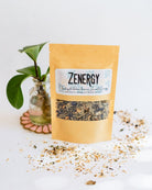 BWG Zenergy tea blend in kraft paper packet with potted plant on beaded coaster and loose tea accents.