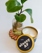 Classy AF Just Because 4oz candle tin with black and gold label, displayed with small potted plant on a pink beaded coaster.