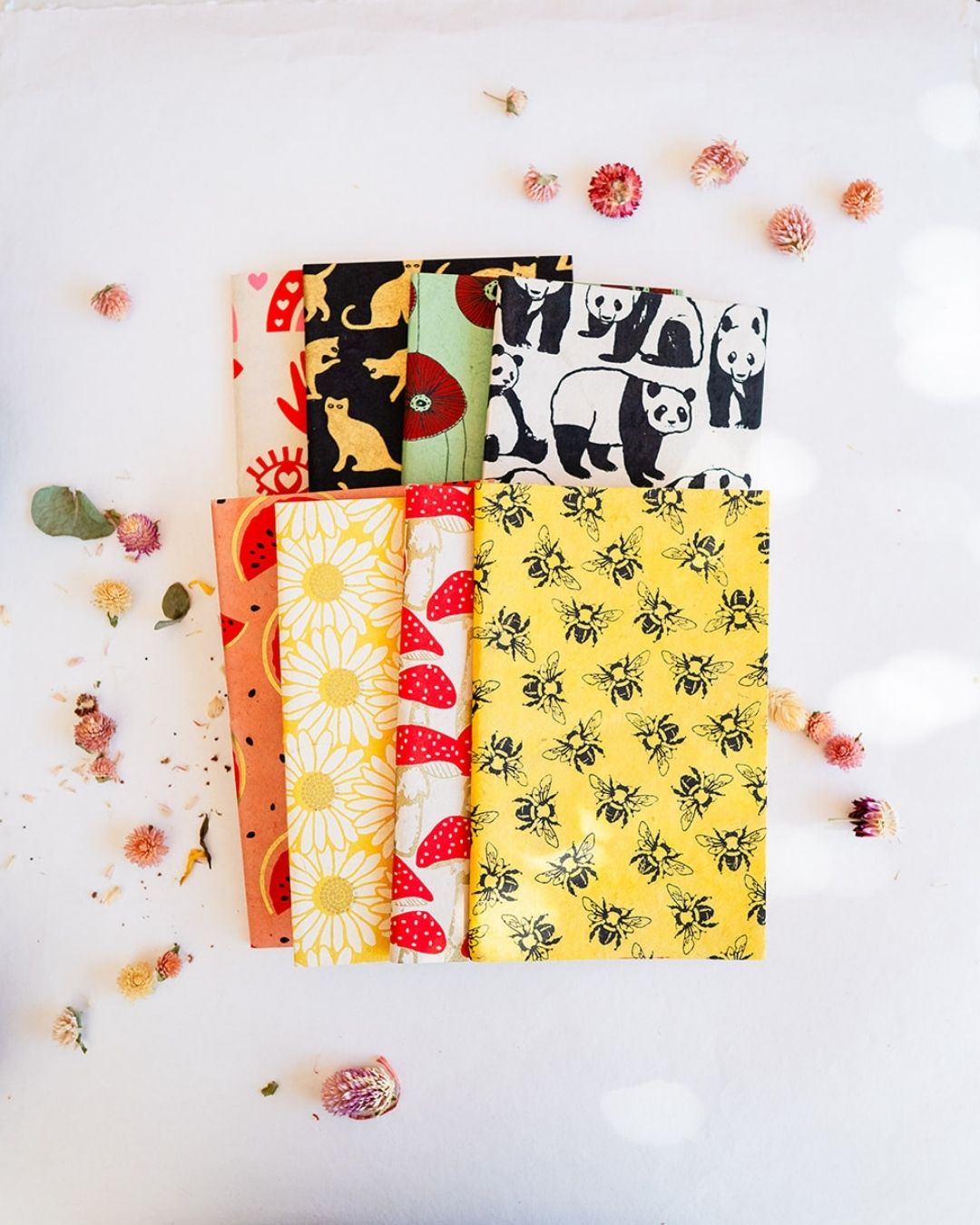 Colorful eco-friendly handcrafted blank journals featuring whimsical mushroom, bee, portrait and flower patterns