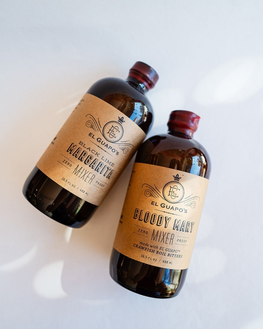 Two El Guapo craft cocktail mixer bottles with vintage-style kraft paper labels on white background.