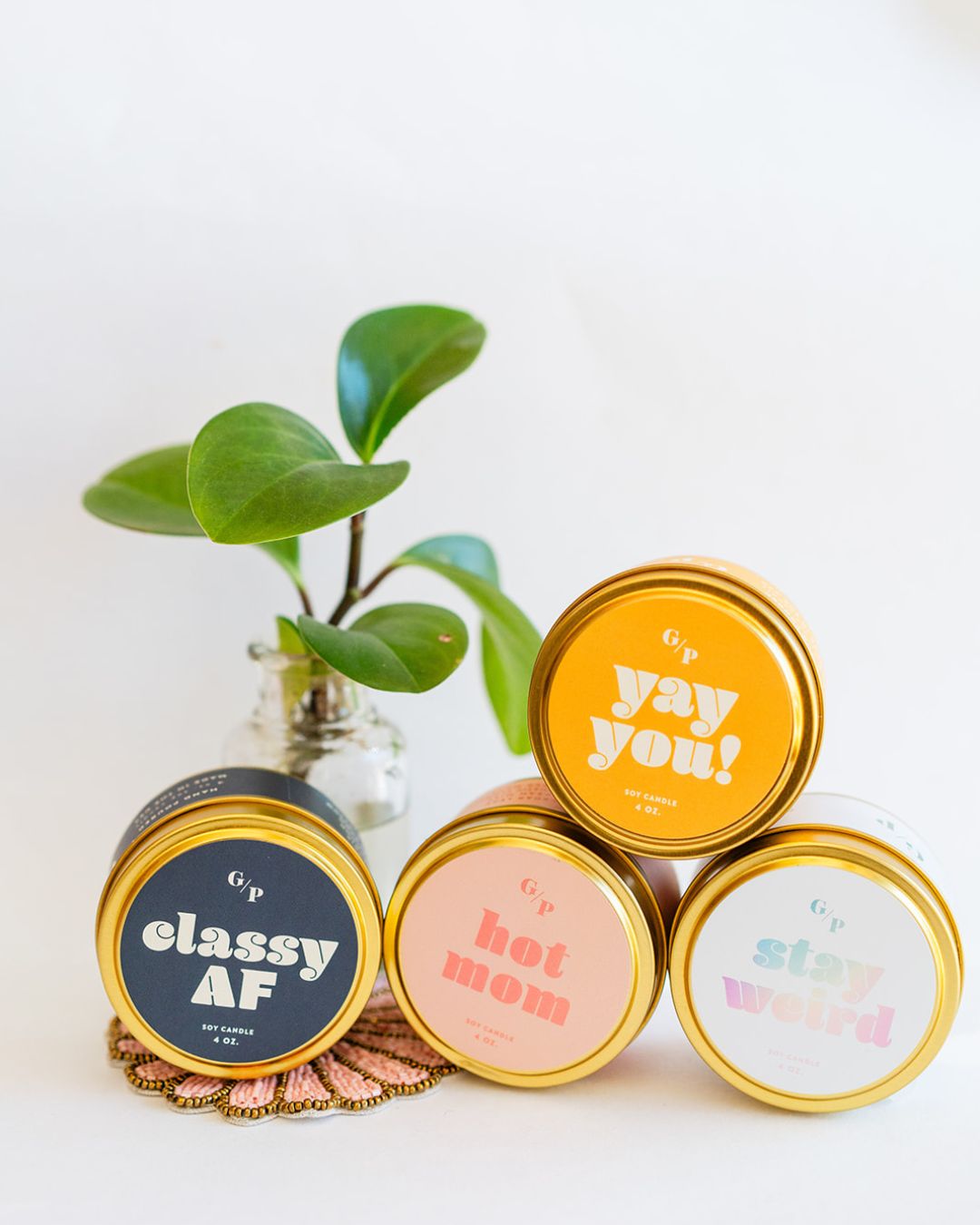 GP Candle Co. 4oz tin collection with Classy AF, Hot Mom, Stay Weird, and Yay You designs with plant
