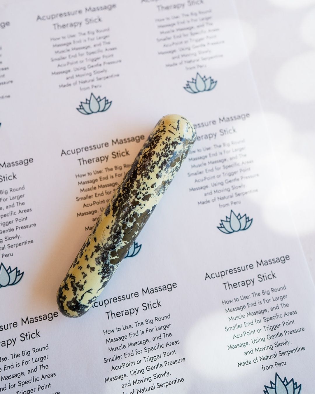 Serpentine stone massage therapy stick with speckled pattern on acupressure card with lotus symbols