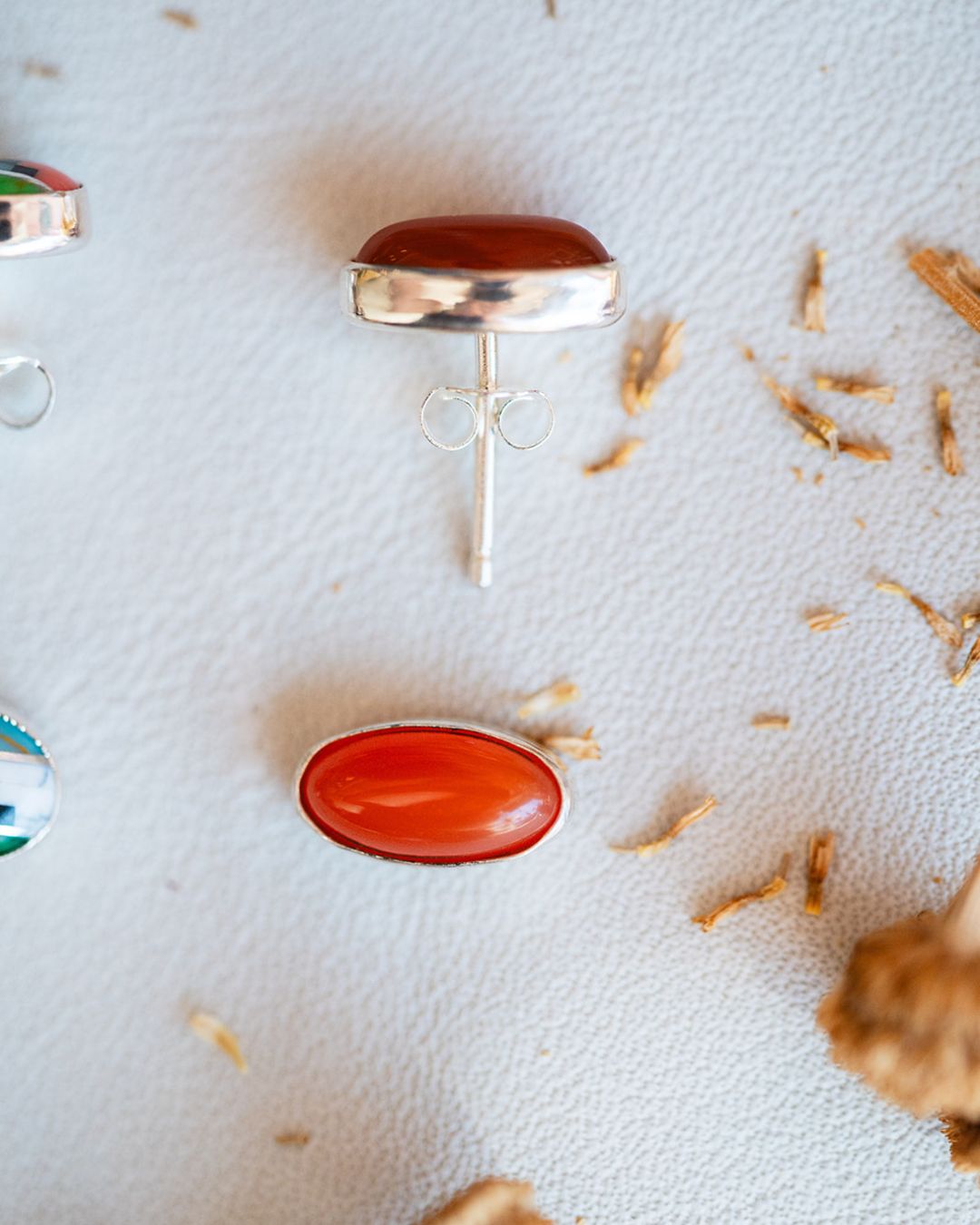 Vibrant orange carnelian oval studs with sterling silver bezels on textured surface