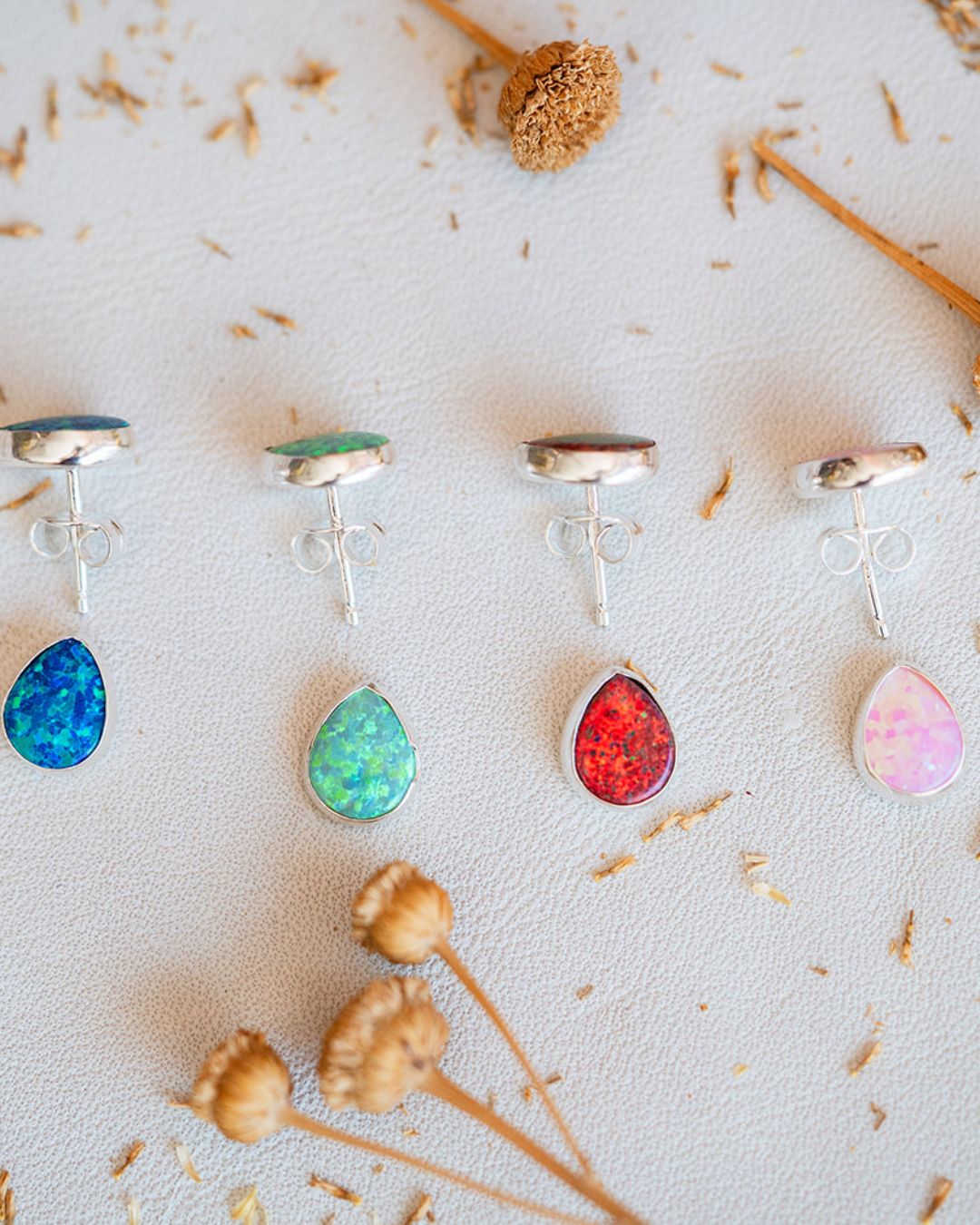 Sterling silver opal studs in blue, green, red, and pink displayed on white surface