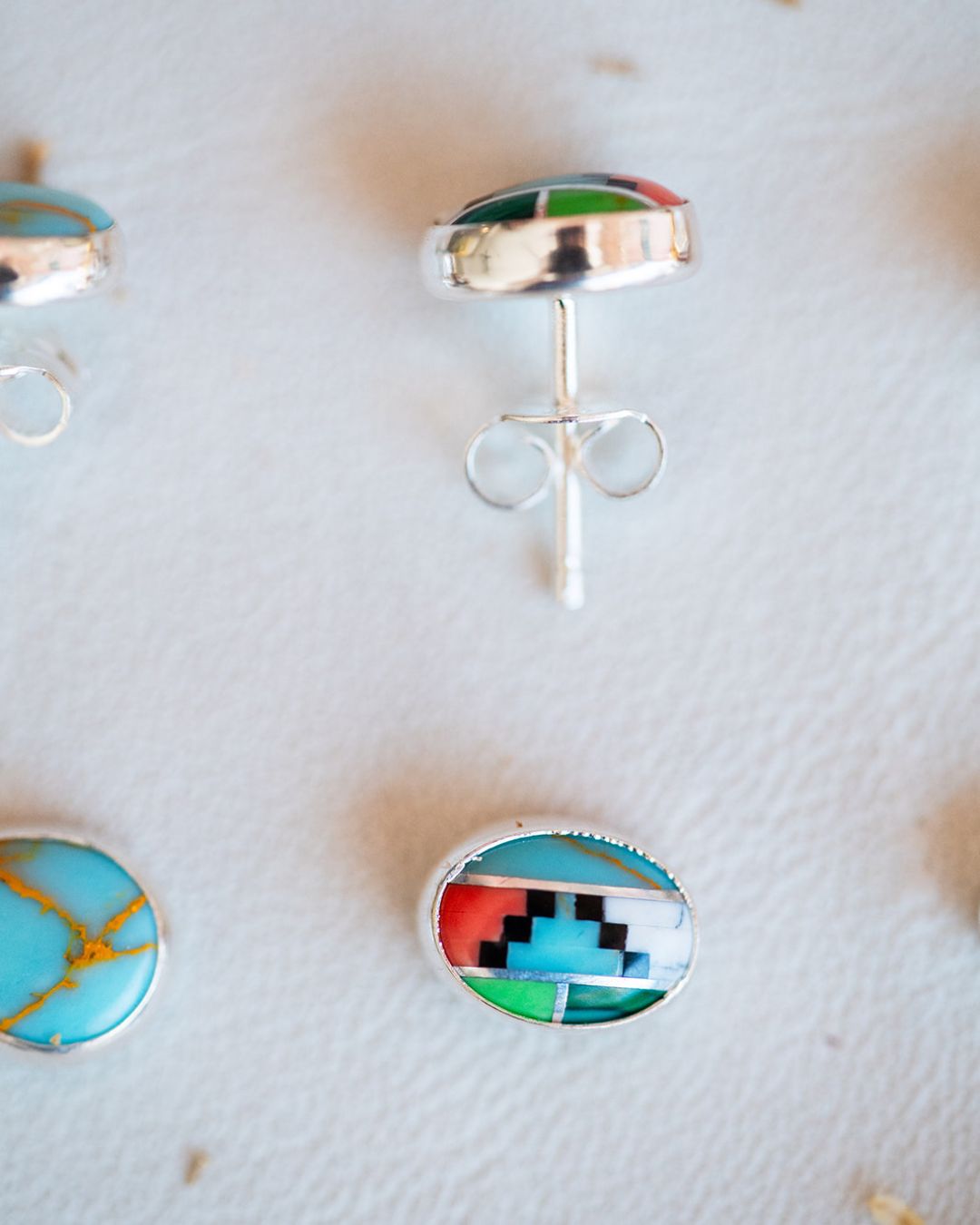 Turquoise oval stud earrings with sterling silver settings on textured surface