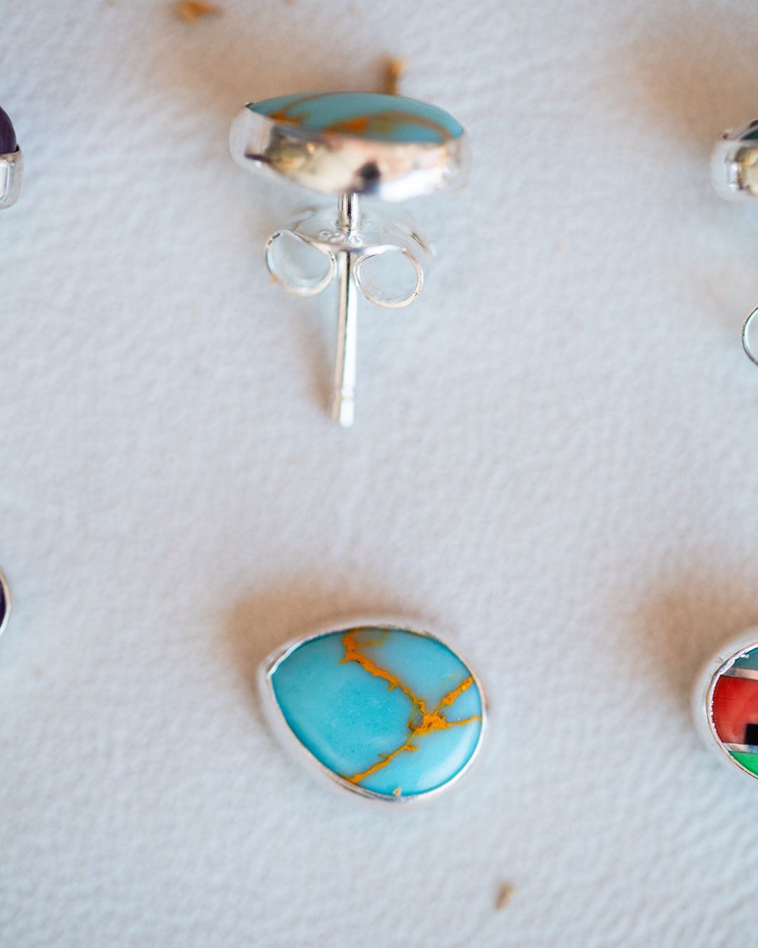 Turquoise oval stud earrings with sterling silver settings on textured surface