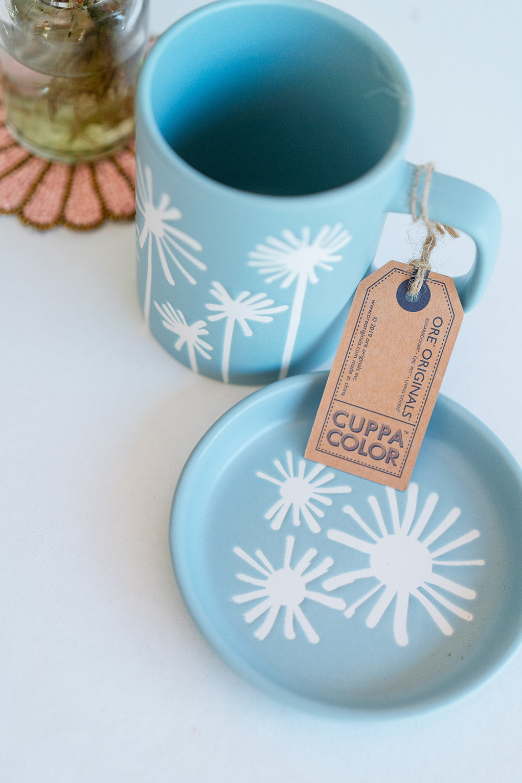 Light blue Cuppa Color ceramic mug and coaster featuring whimsical white dandelion silhouette design, handcrafted premium ceramic set.