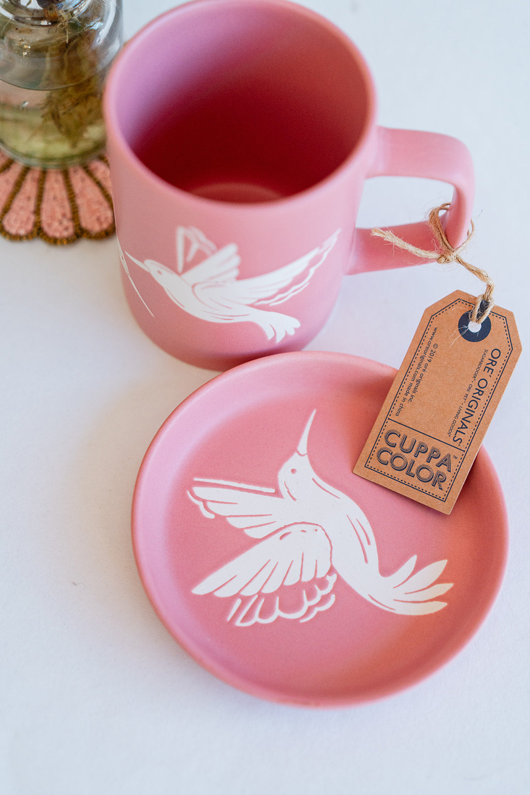 Handcrafted pink Cuppa Color ceramic mug and matching coaster with white hummingbird silhouette design, includes artisanal hang tag.