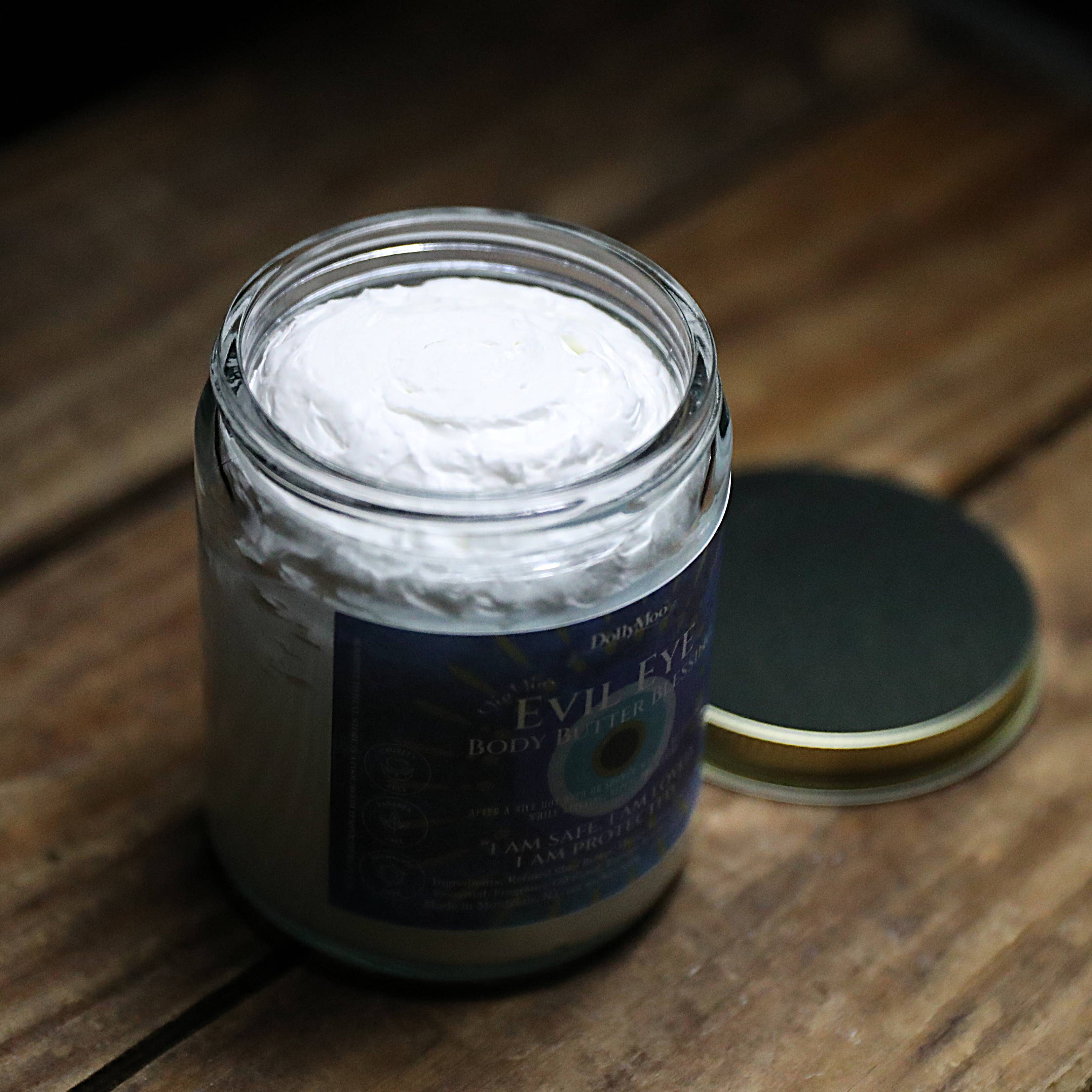 Open jar of DollyMoo Evil Eye Body Butter showing rich organic shea and mango butter blend with protective essential oils and creamy texture
