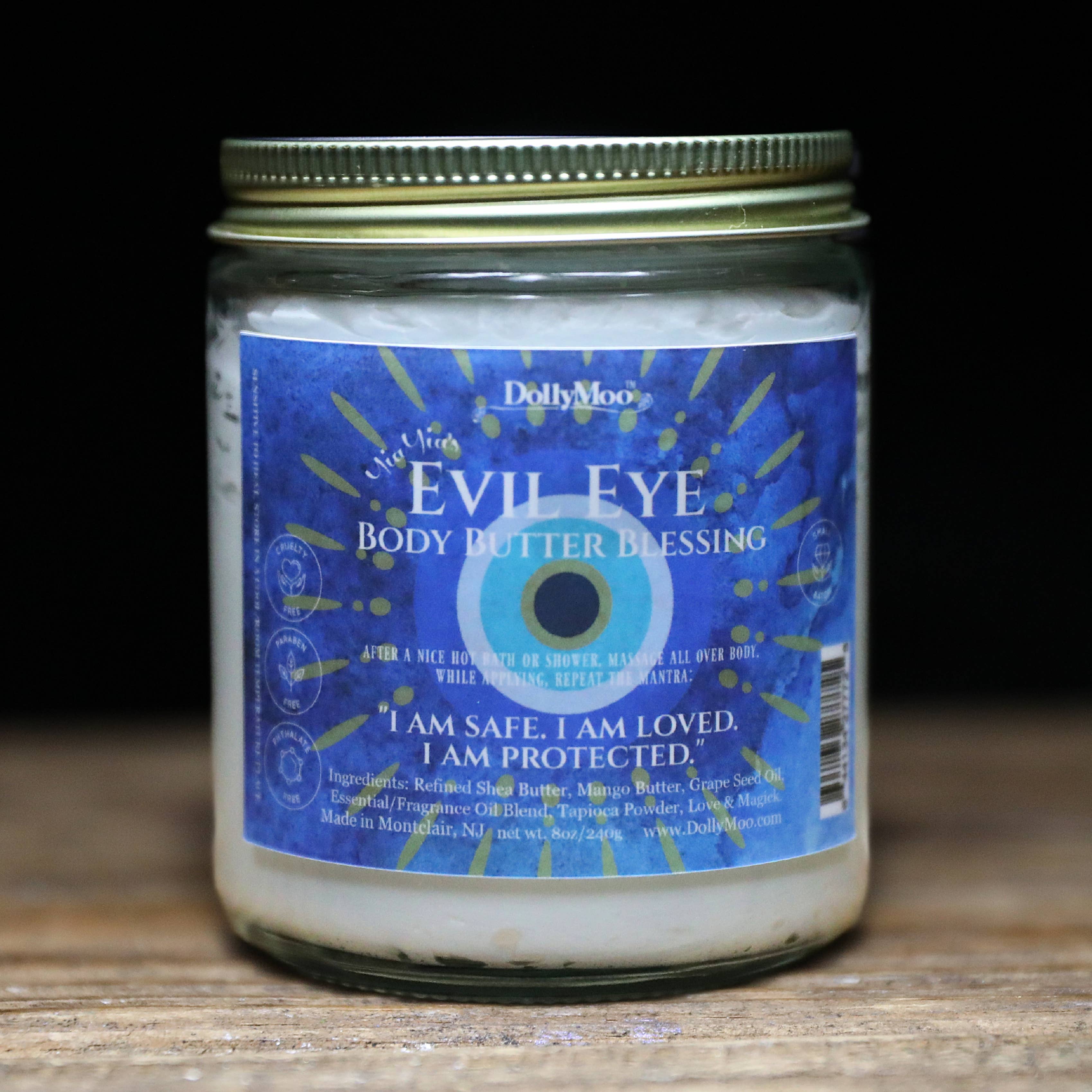 DollyMoo Evil Eye Body Butter blessing in 8oz jar featuring traditional blue protection symbol with affirmation 'I am safe, I am loved, I am protected' on label.