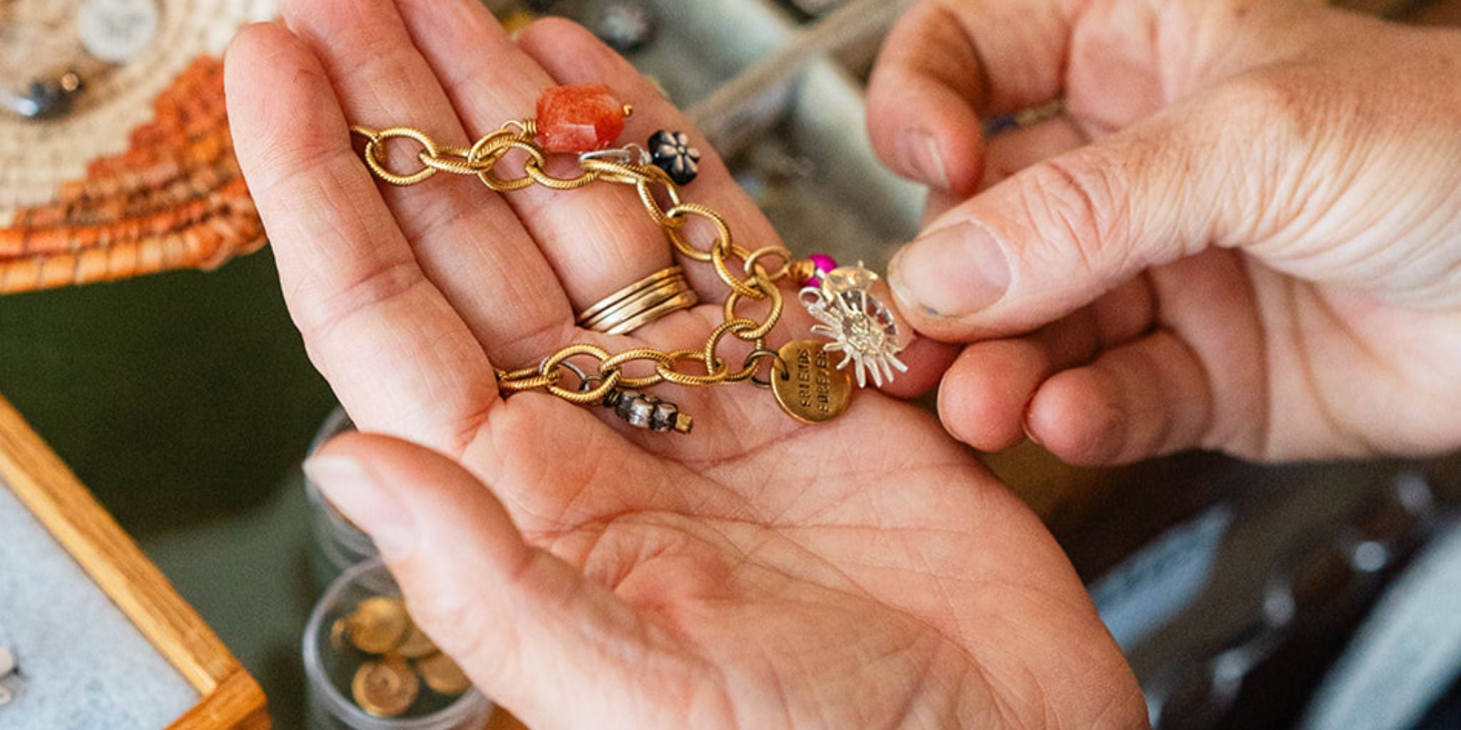 Hands sharing a handcrafted gold charm bracelet with personalized charms including a 'sisters' charm, showcasing Bella Vita Jewelry's custom milestone jewelry made in Little Rock, Arkansas