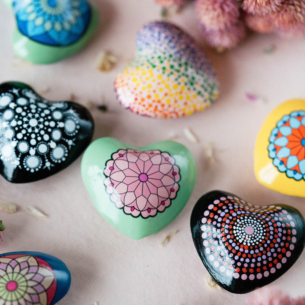 Close-up of decorative mandala chime hearts showing detailed handpainted dot patterns and floral mandalas in green, black, rainbow and yellow colors.