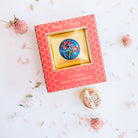 Song of India Love natural solid fragrance in red box with gold lattice pattern, showcasing blue background brass container with vibrant floral design.